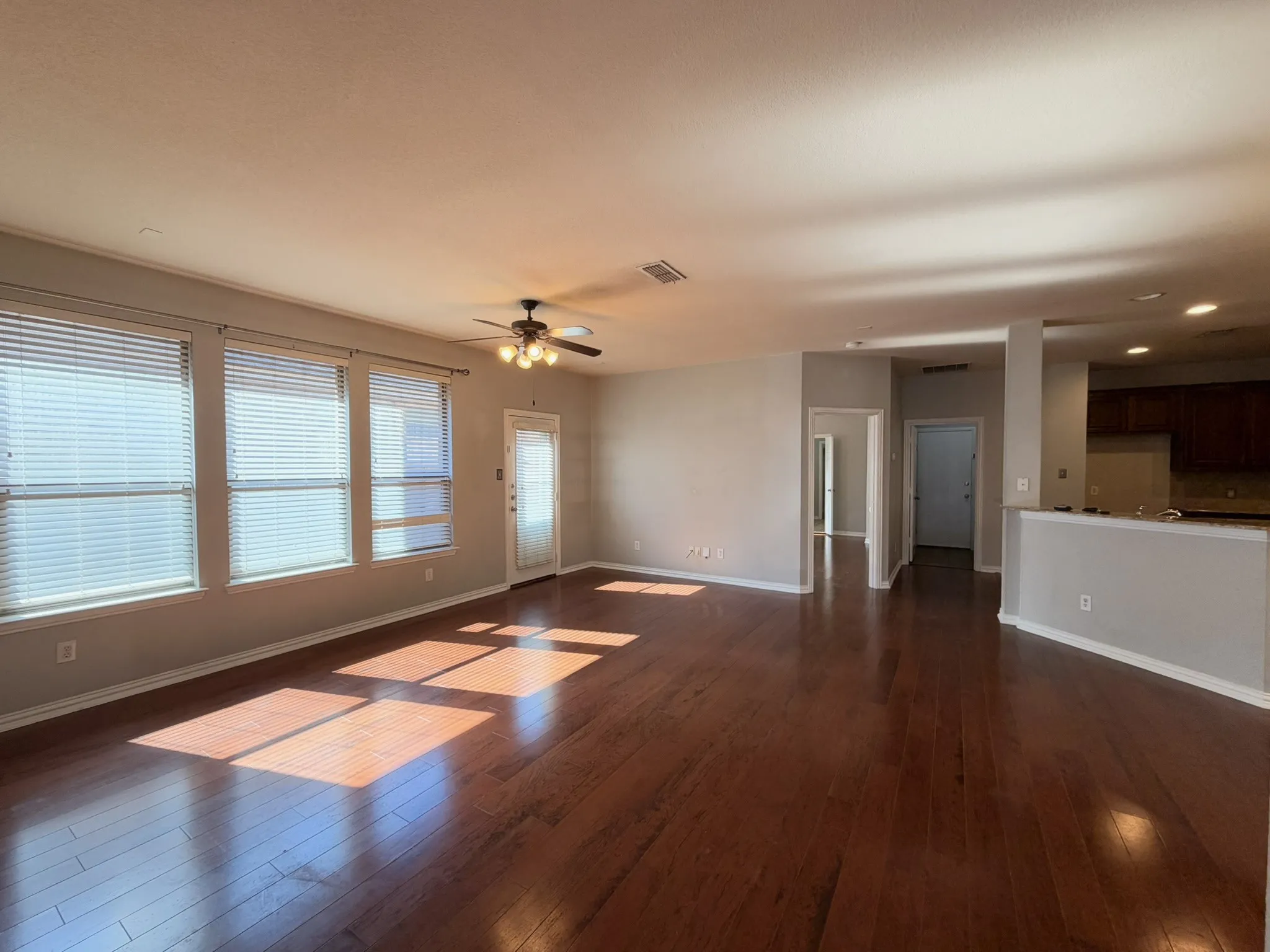 Hardwood flooring, multiple windows with blinds, ceiling fan with integrated lighting, a glass-paneled door, and a partial view of kitchen cabinetry