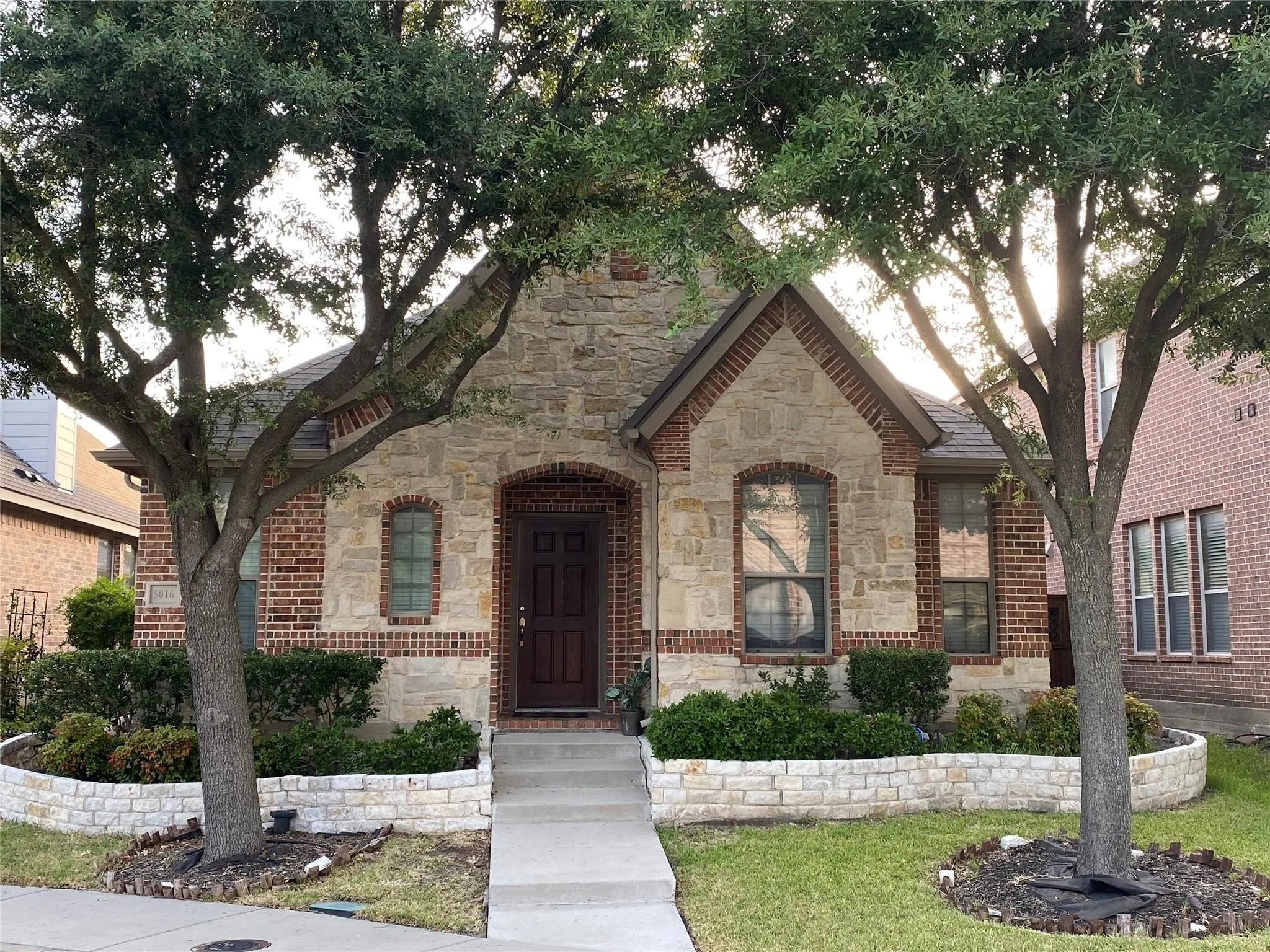 Stone and brick facade with dark wood entry door, arched brick accents, and a concrete pathway