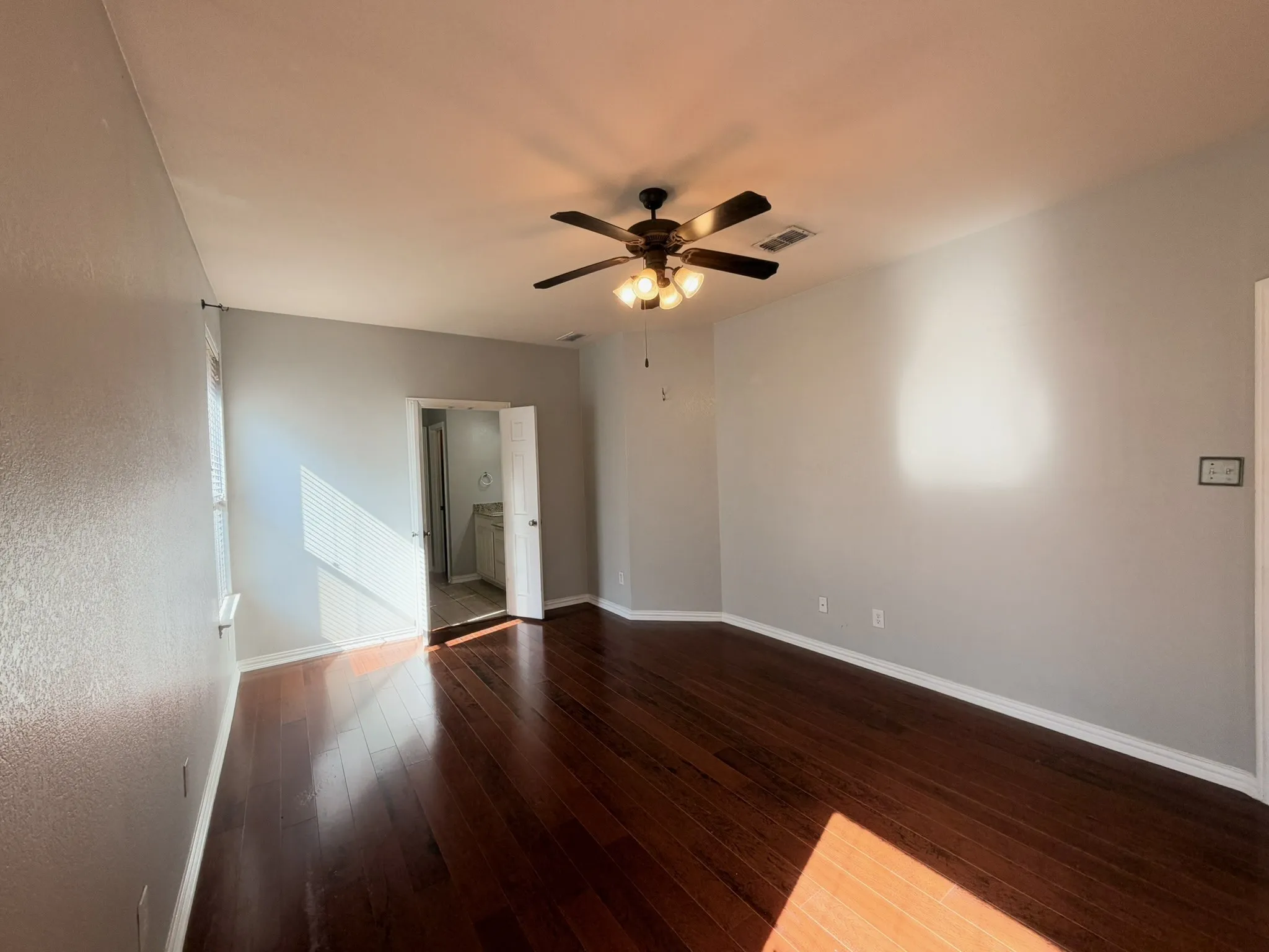 Rich wood-finish flooring, ceiling fan with integrated lighting, and neutral wall tones