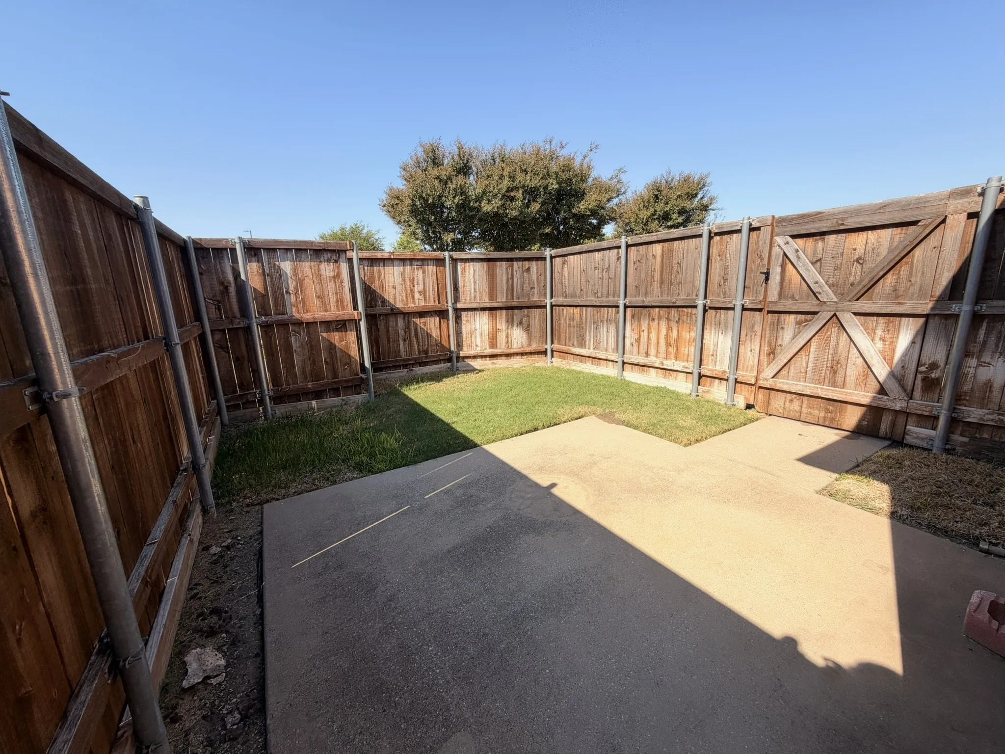 Fenced outdoor space featuring a concrete patio, grassy area, and wood panel fencing