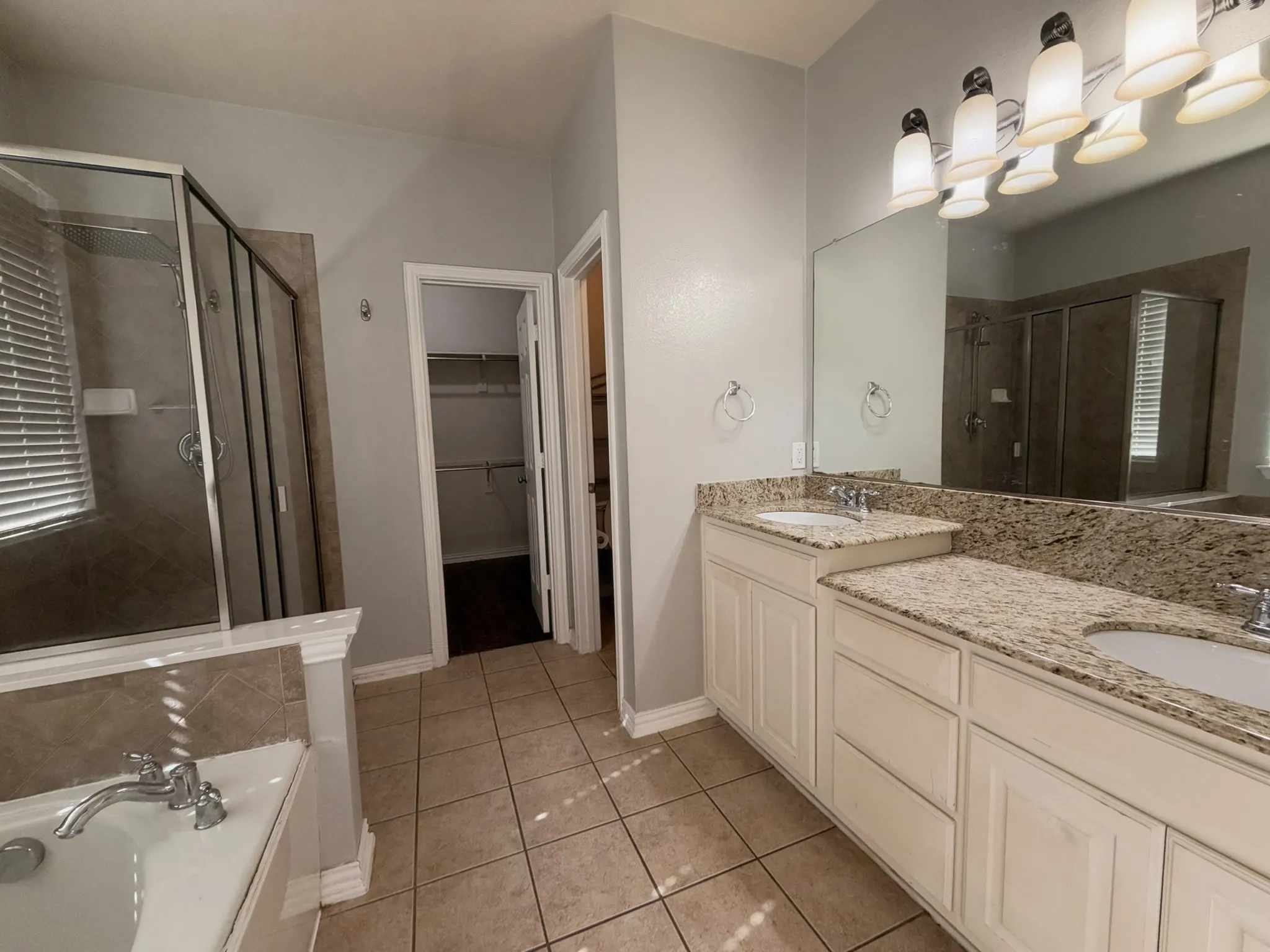Dual vanity with light-colored countertops, tile flooring, built-in bathtub, and a glass-enclosed shower