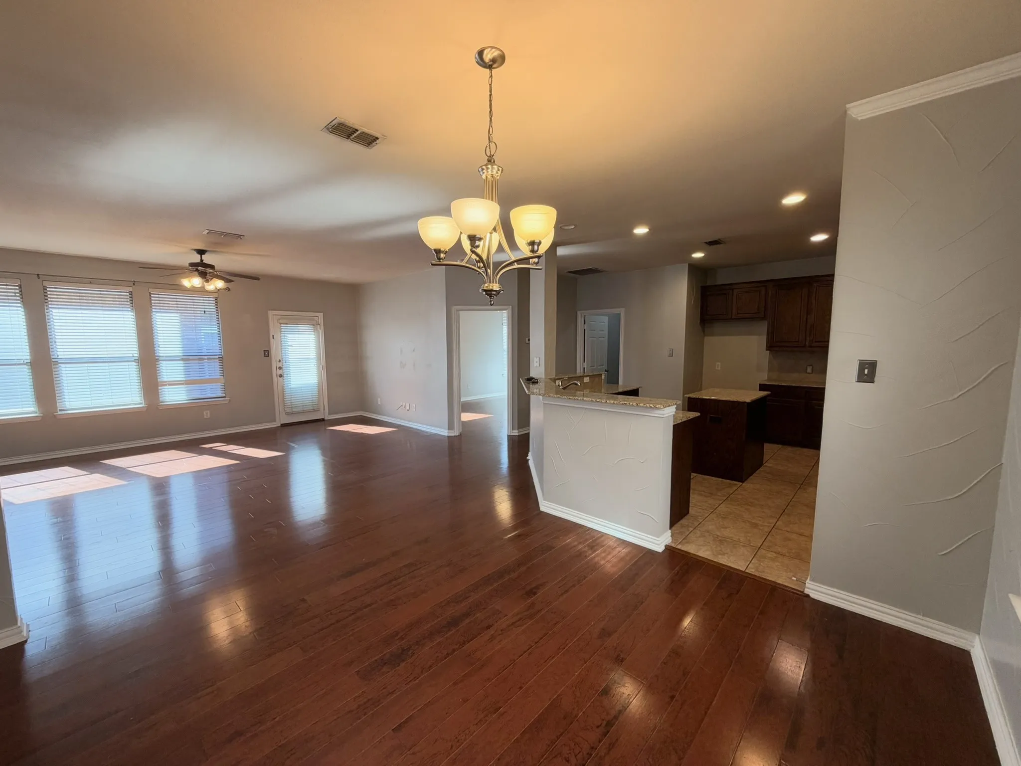 Expansive living area with wood-finish flooring, multiple windows, and a ceiling fan