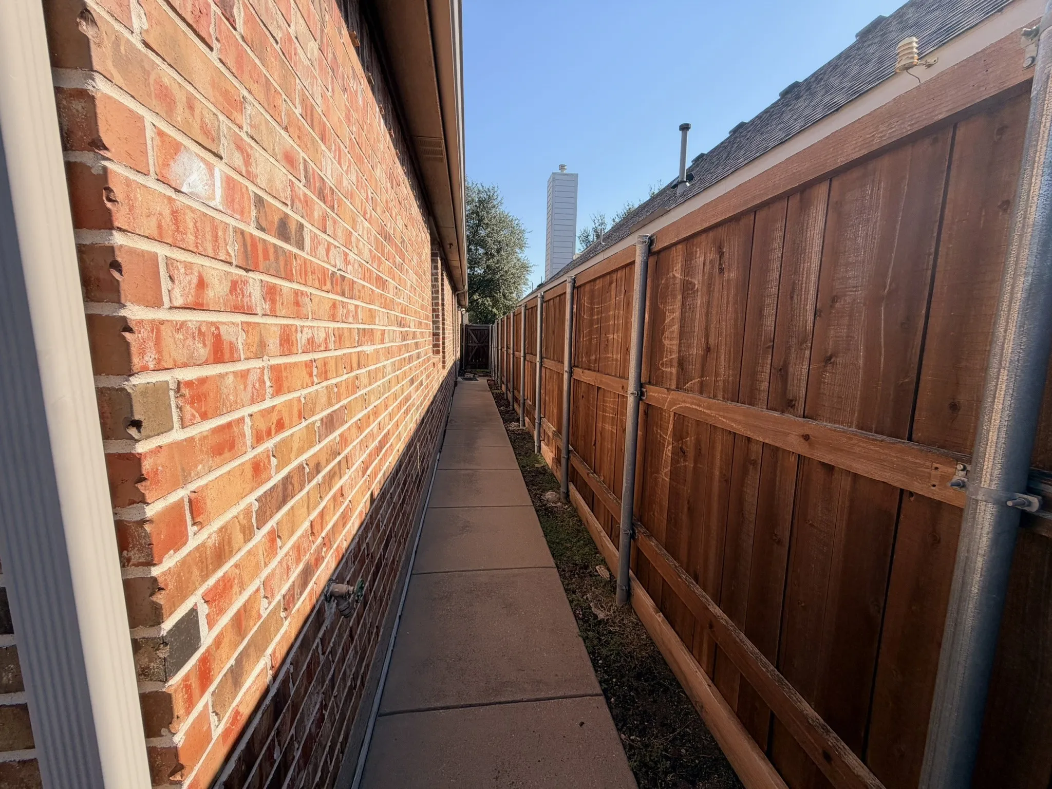 Brick exterior with a concrete pathway and wood-panel fencing