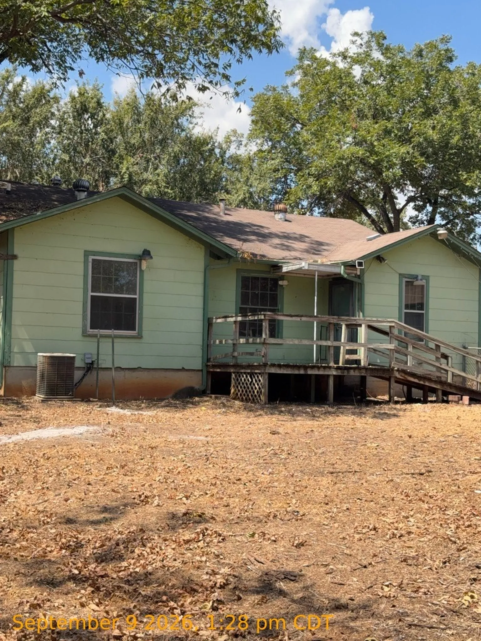 Rear exterior with light green siding, elevated wood deck, and an accessible ramp