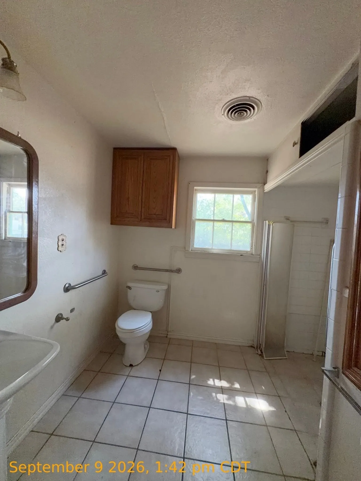 Pedestal sink, wall-mounted wood-finish cabinetry, tile flooring, and a single window for natural light