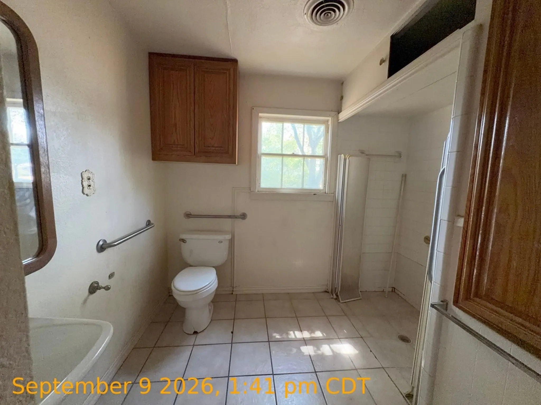 Bathroom featuring a window, tile flooring, a built-in shower, a wall-mounted sink, and wooden cabinetry