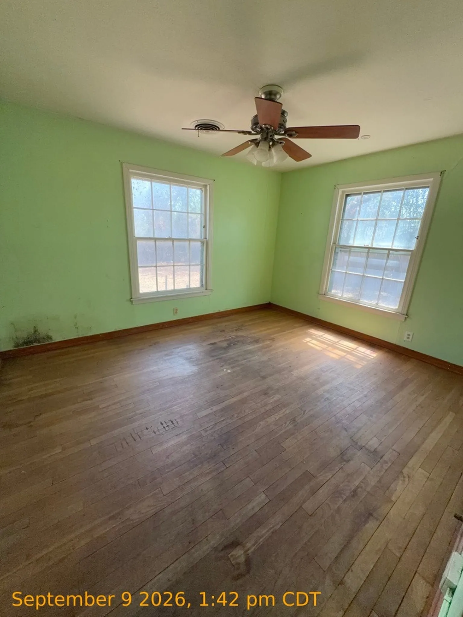 Wood-finish flooring with dual windows and a ceiling fan with integrated lighting