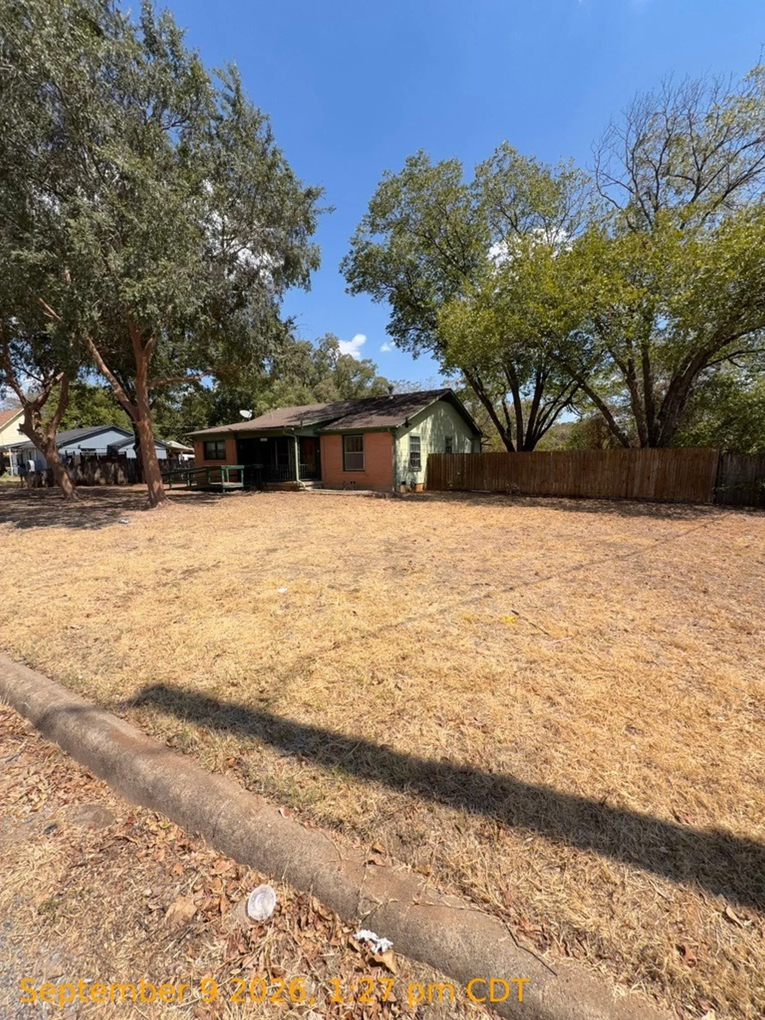 Front yard with mature trees, a partial privacy fence, and a single-story residence featuring a covered porch