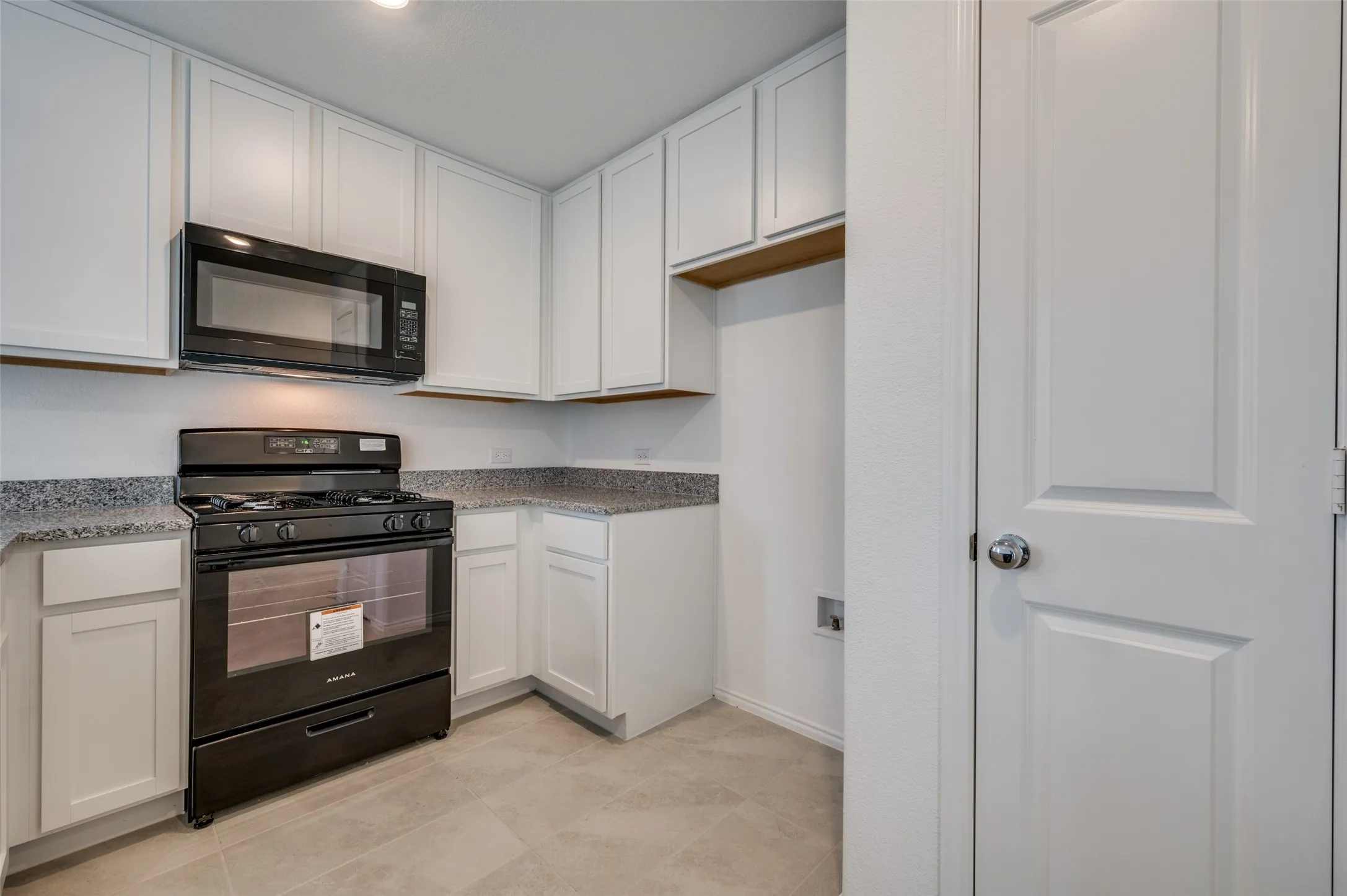 Kitchen featuring black appliances, white cabinets, and light tile floors