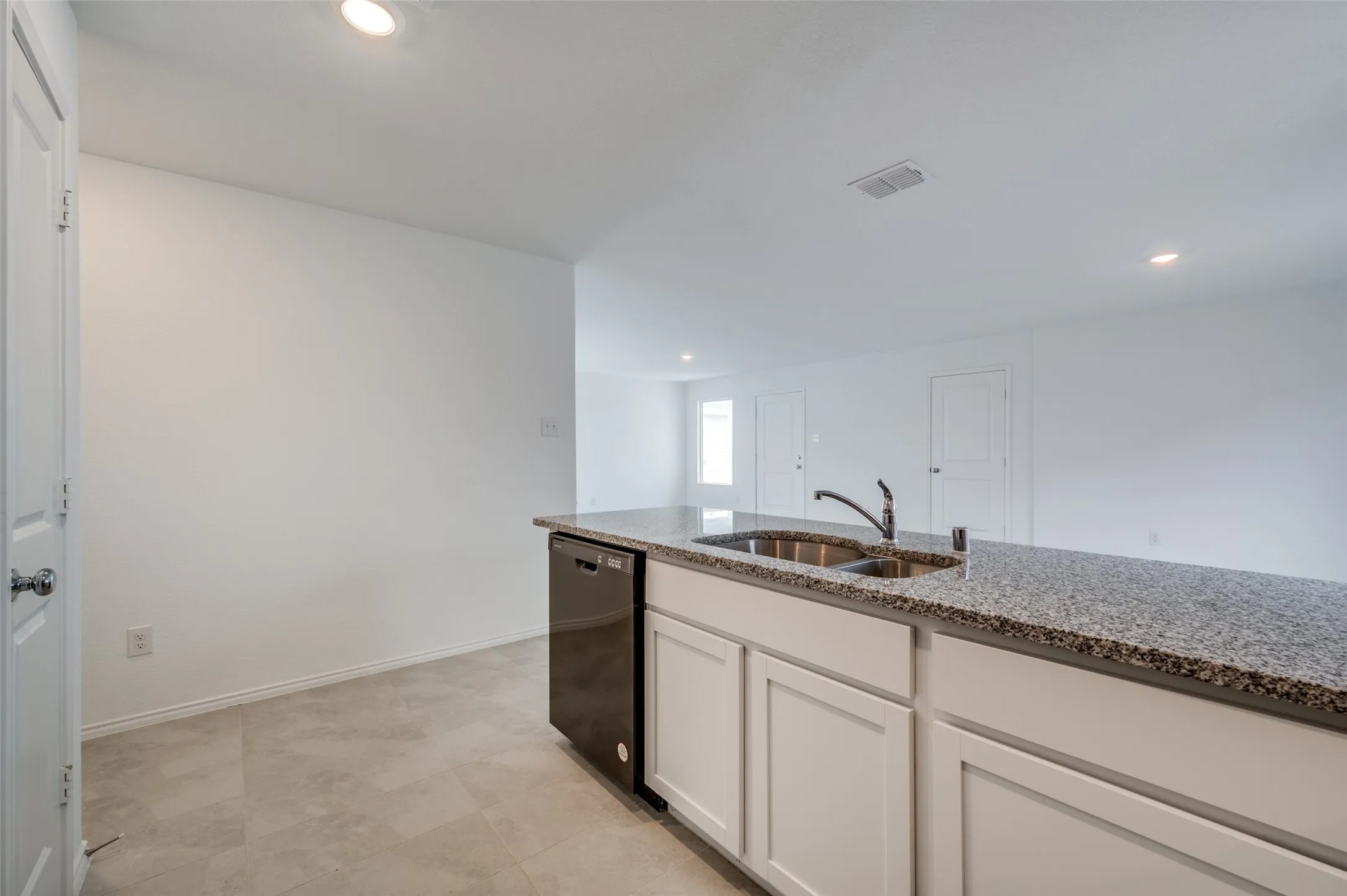 Kitchen with white cabinets, light stone counters, dishwasher, sink, and light tile floors