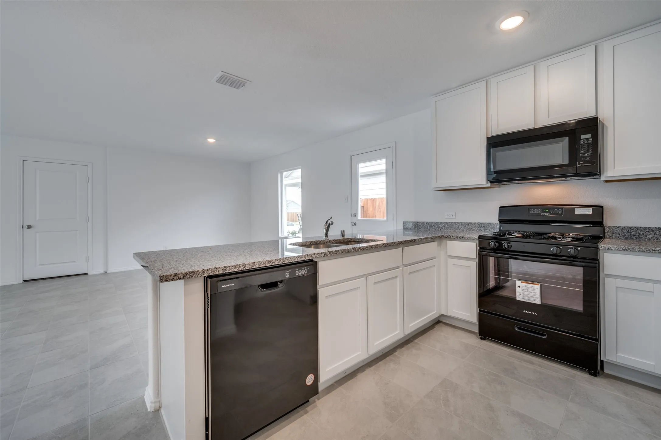 Kitchen with white cabinetry, black appliances, light tile floors, and kitchen peninsula
