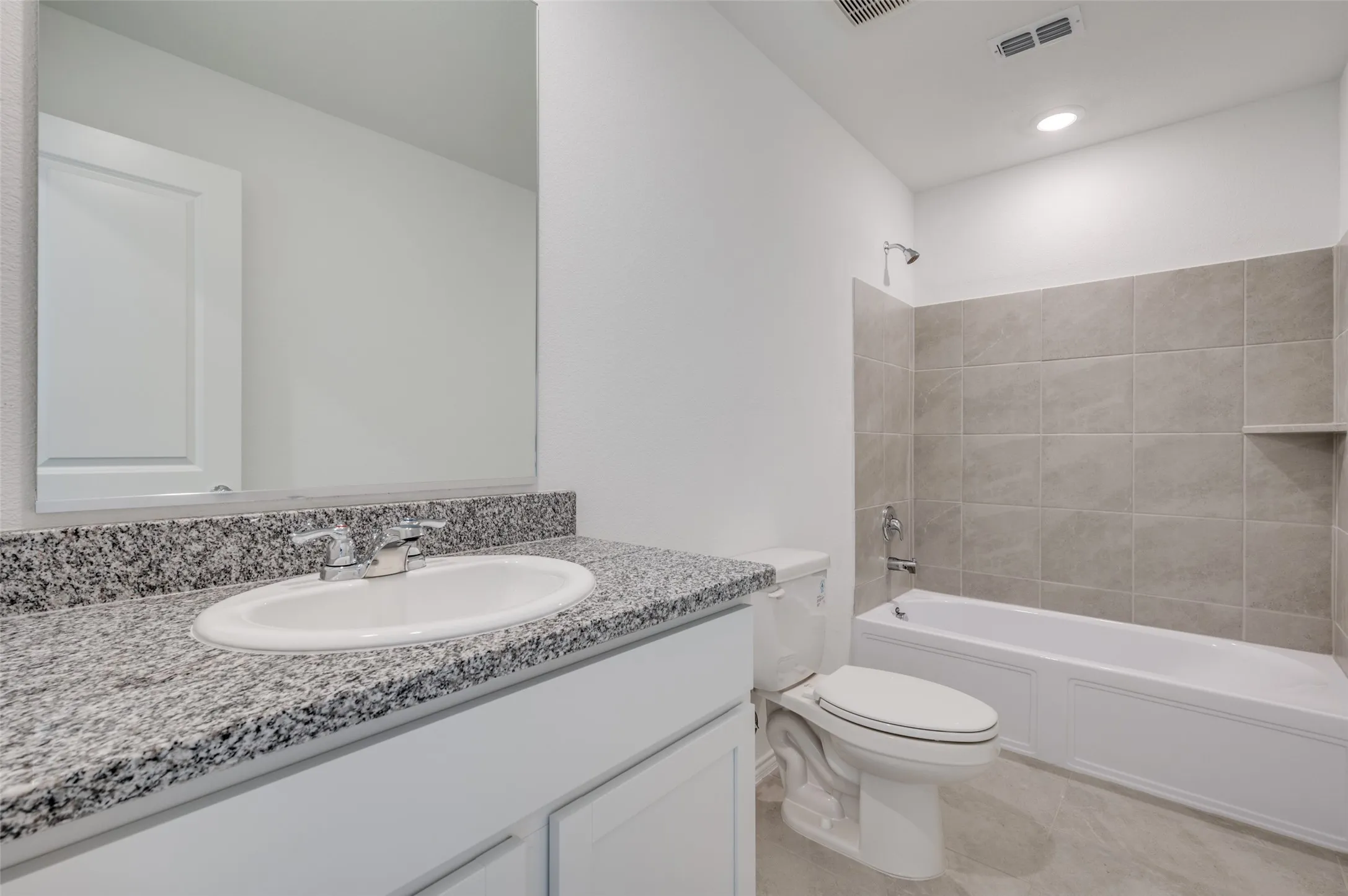 Full bathroom with tile floors, tiled shower / bath combo, large vanity, and toilet