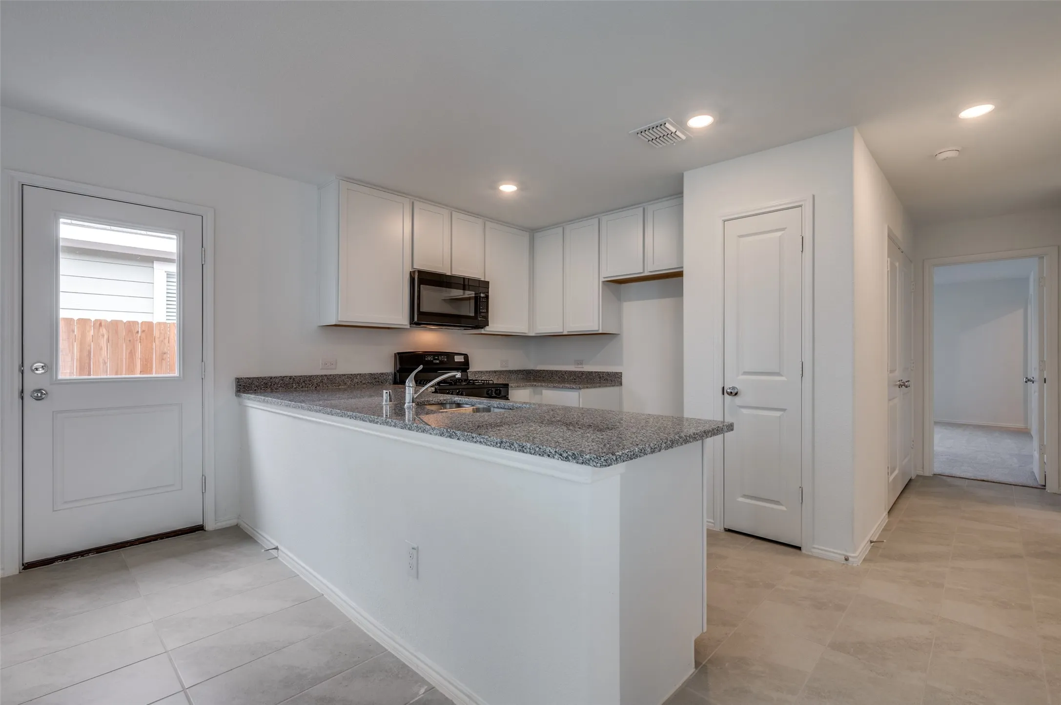 Kitchen with black appliances, white cabinets, kitchen peninsula, and light tile floors