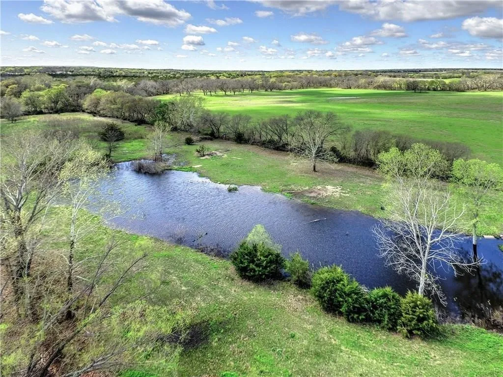 Expansive green pastures and mature trees surround a tranquil pond