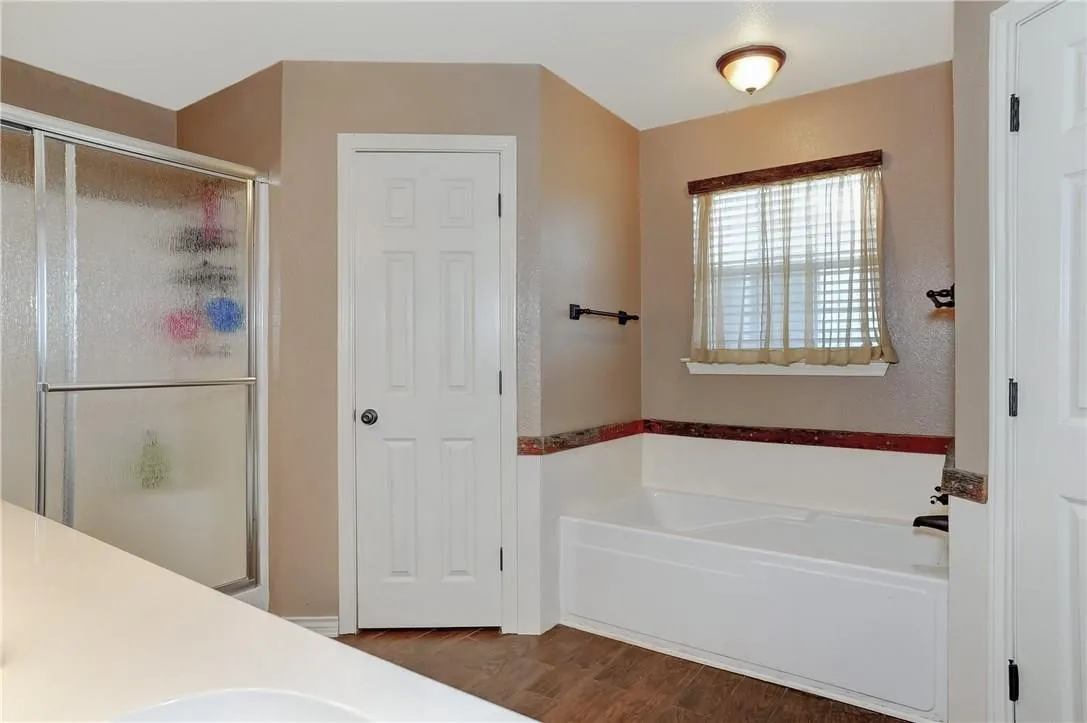 Shower enclosure with sliding glass door, white bathtub, wood-finish flooring, and a white six-panel door