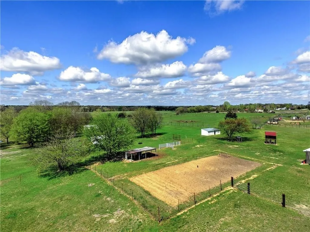 Expansive green acreage featuring mature trees, a fenced paddock, and multiple outbuildings