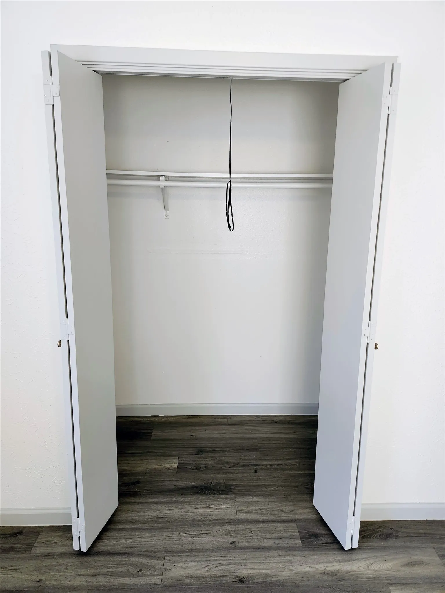 Bi-fold closet doors revealing an interior storage rod and shelving, with wood-finish flooring