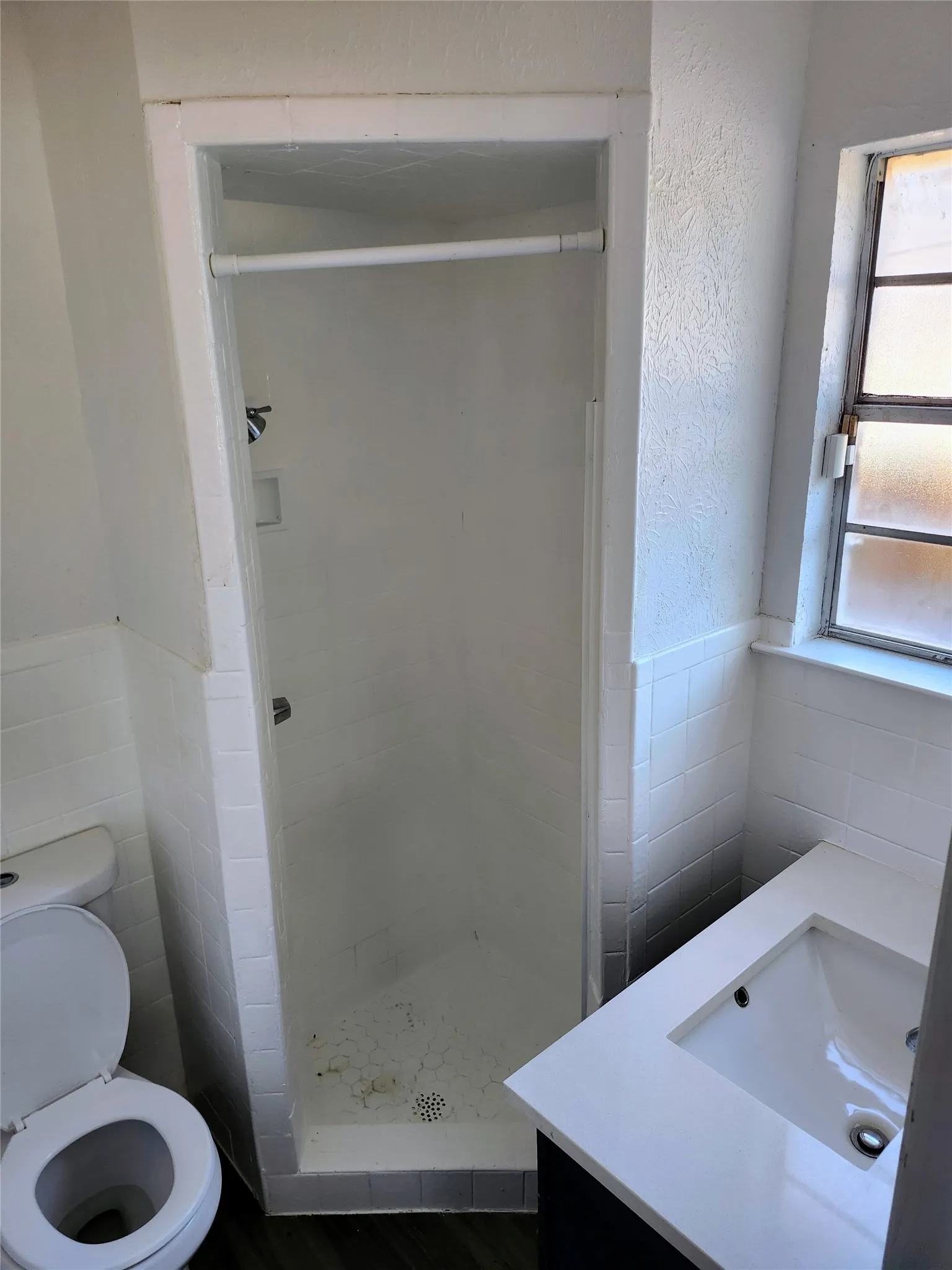 Built-in shower stall with white tile surround, white toilet, and vanity with integrated sink