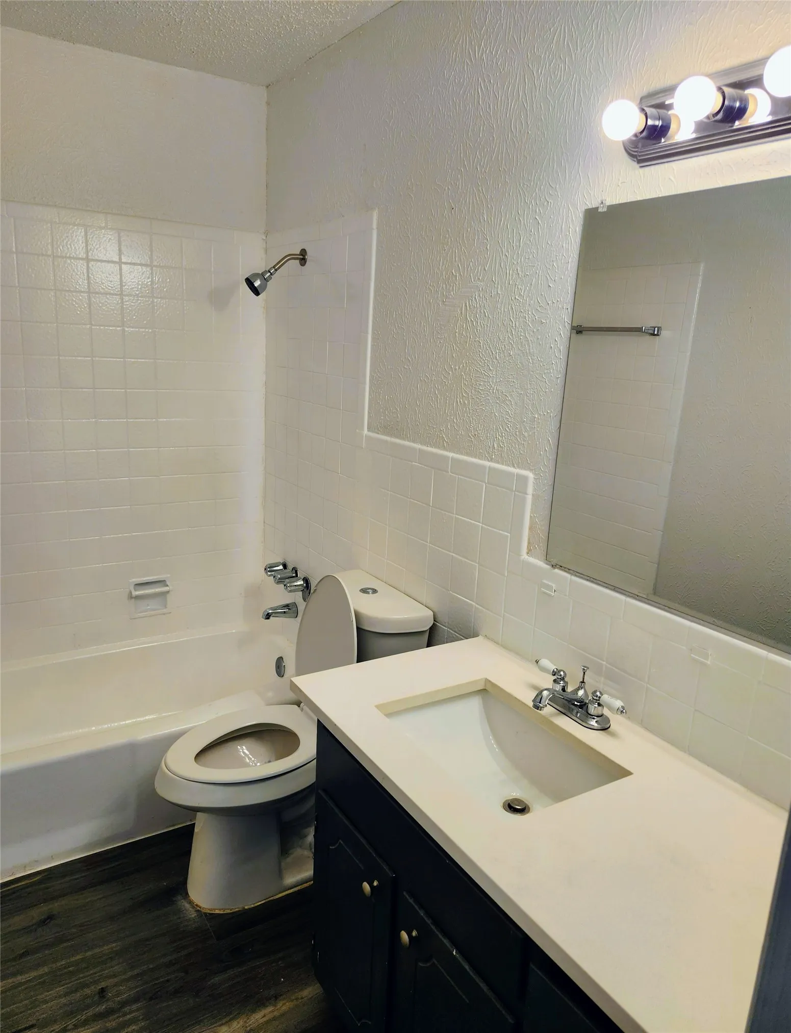 Bathroom featuring a white subway tile tub surround, white vanity countertop, integrated sink, dark wood-finish vanity cabinetry, and wood-finish flooring
