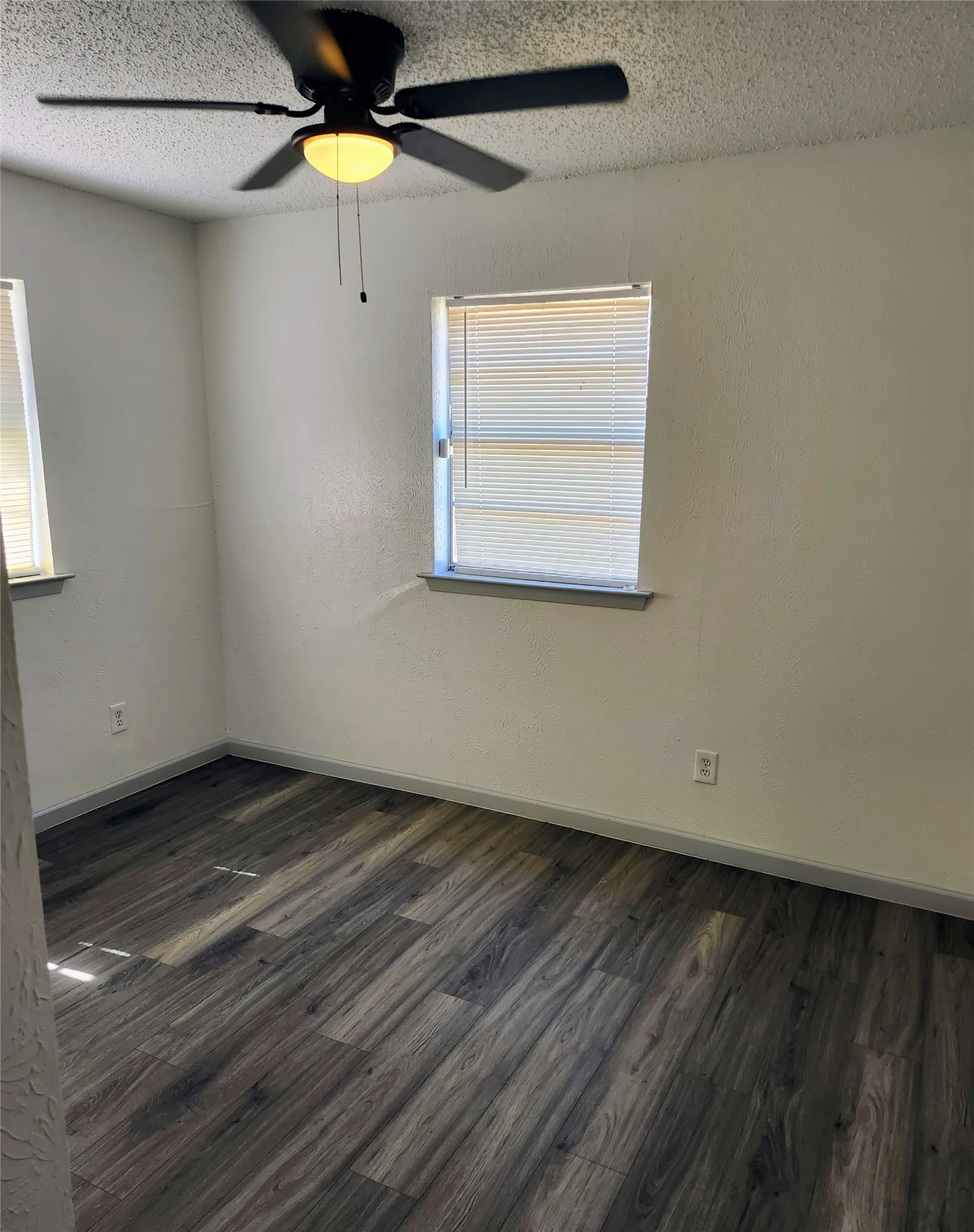 Guest Bedroom #1 - Wood-finish flooring, two windows with blinds, and a ceiling fan with integrated lighting