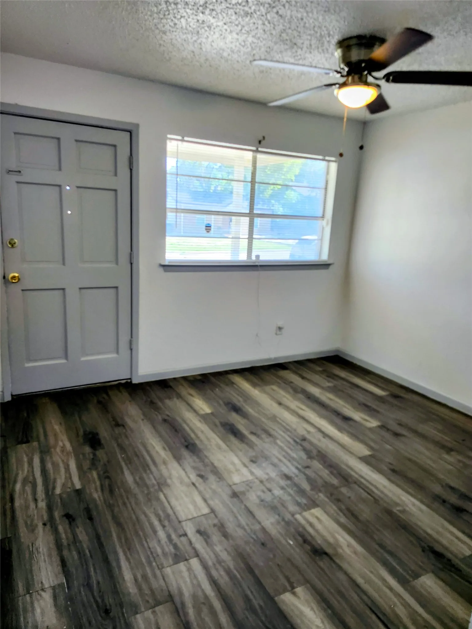 Living Room - Wood-finish flooring, paneled entry door, window with blinds, and a ceiling fan with integrated lighting
