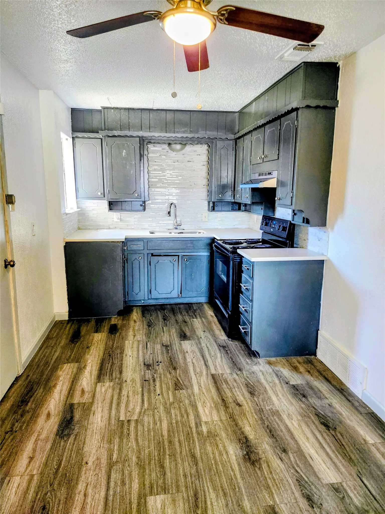 Kitchen featuring wood-finish flooring, white subway tile backsplash, dark cabinetry, and white countertops