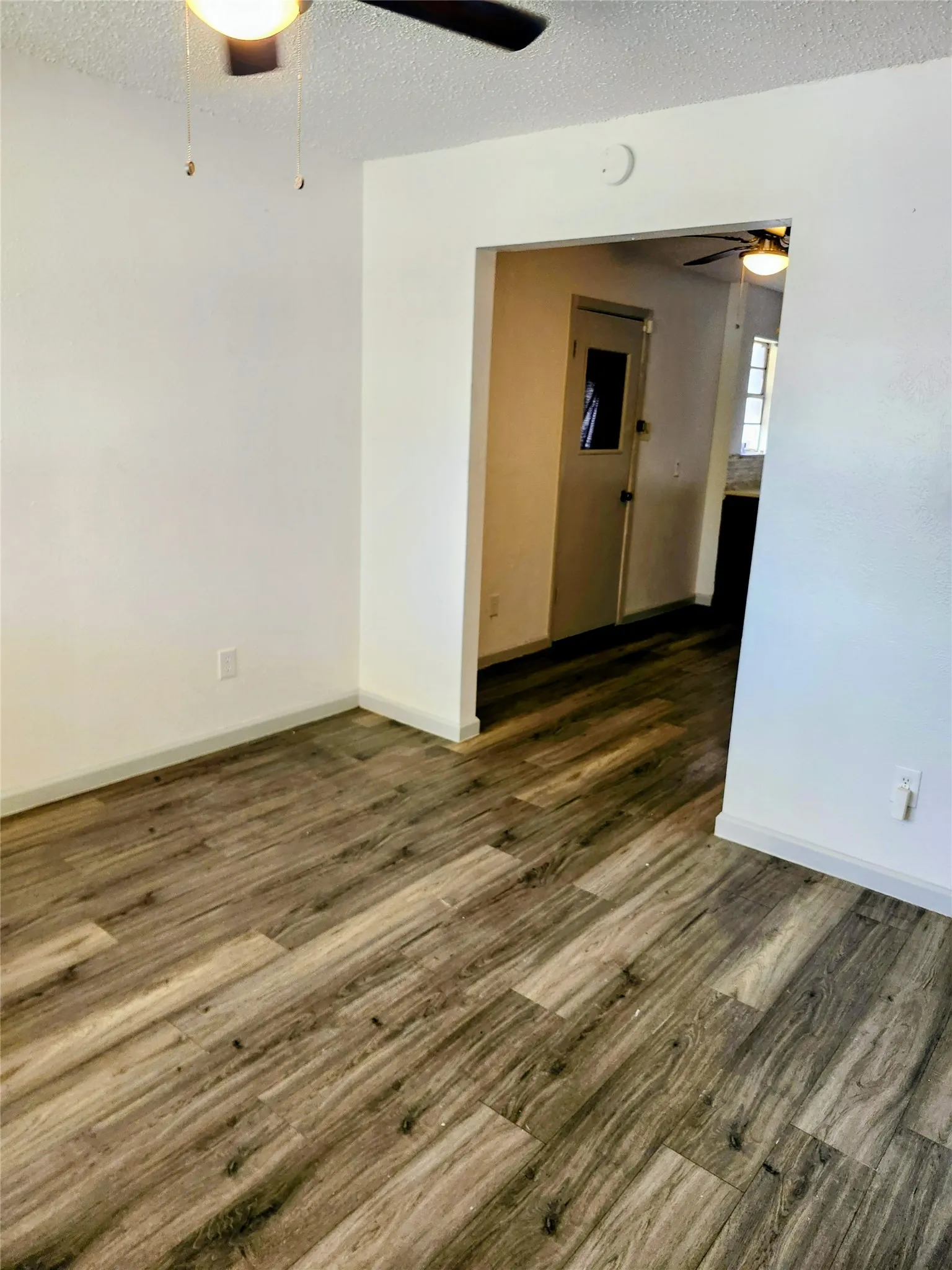 Living room to Kitchen. Wood-finish flooring with white baseboards, featuring an overhead ceiling fan
