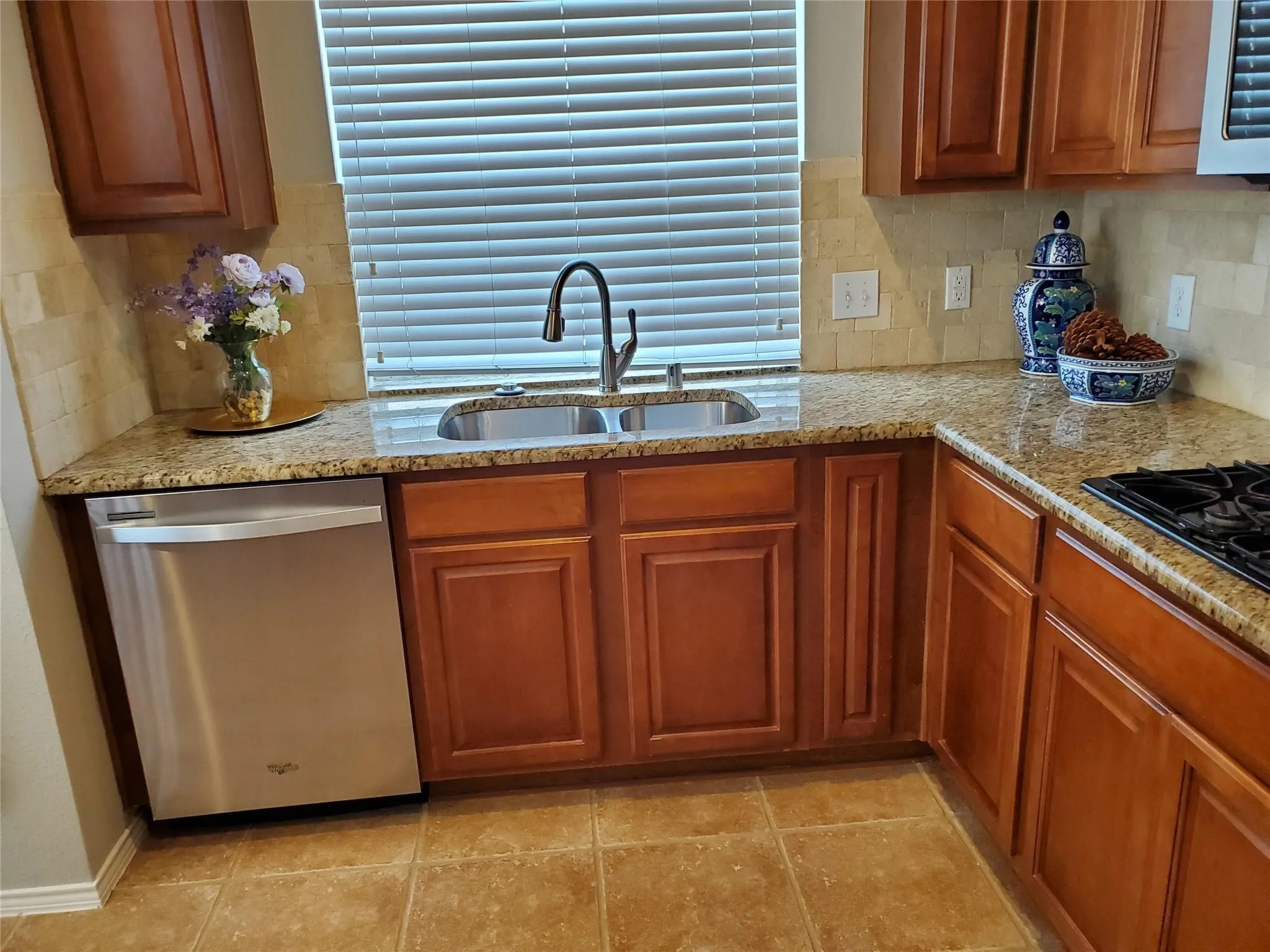 Kitchen featuring light tile patterned flooring, dishwasher, backsplash, light stone counters, and sink