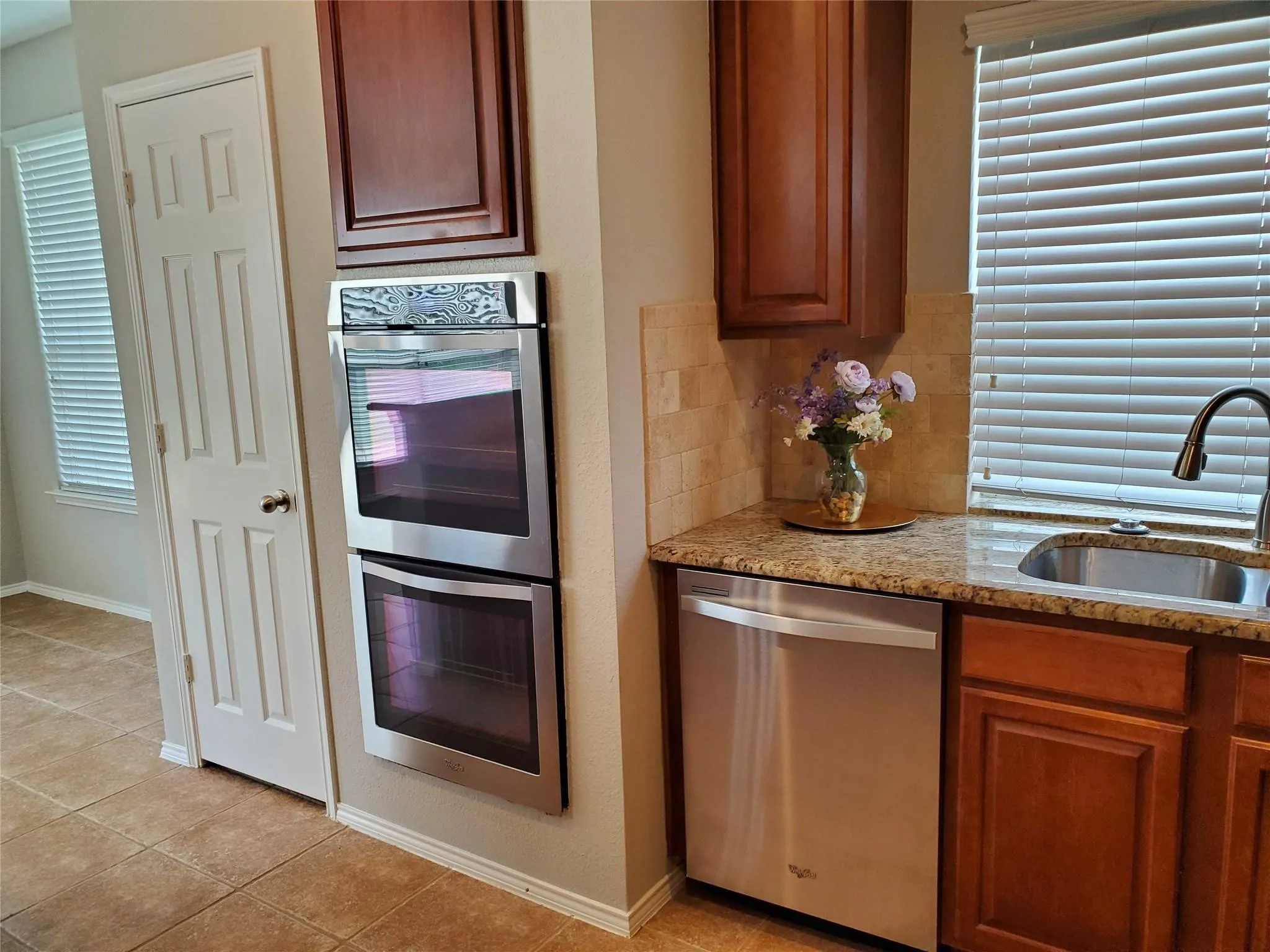 Kitchen with light stone counters, appliances with stainless steel finishes, light tile patterned flooring, backsplash, and sink