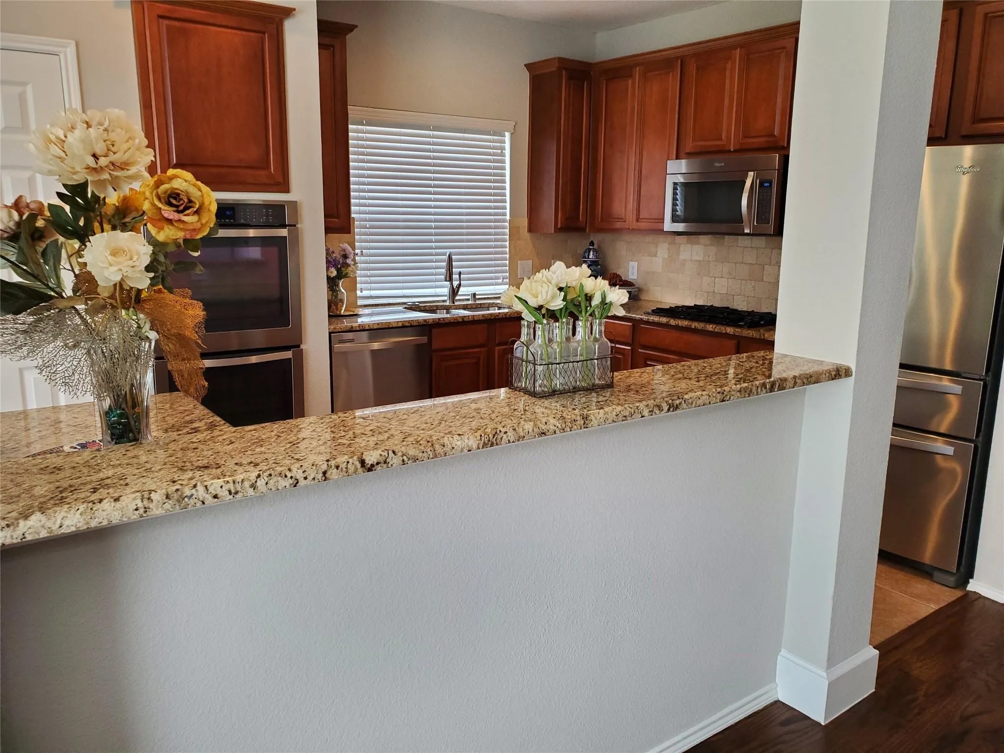 Kitchen featuring dark wood-type flooring, appliances with stainless steel finishes, sink, tasteful backsplash, and light stone counters