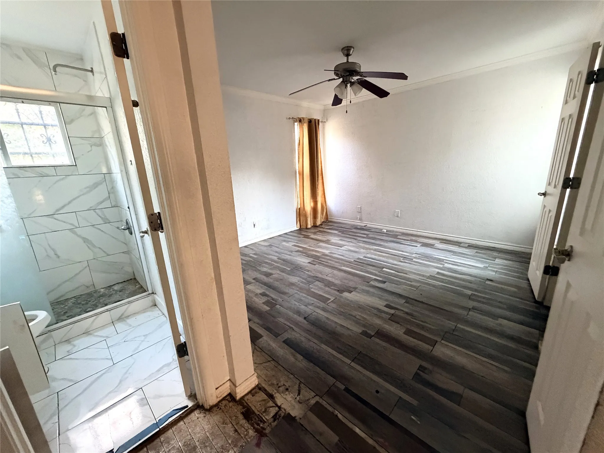 Wood-finish flooring with crown molding, ceiling fan, and an en-suite bathroom featuring a glass-enclosed shower with tiled walls and flooring