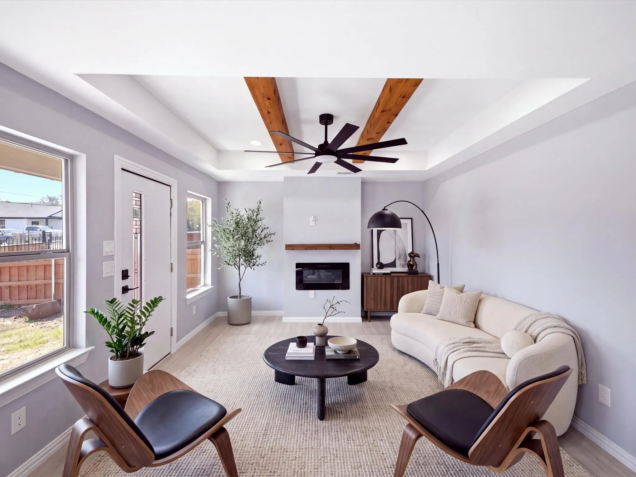 Tray ceiling with wood beam accents, ceiling fan, contemporary fireplace with wood mantel, wood-finish flooring, and white trim
