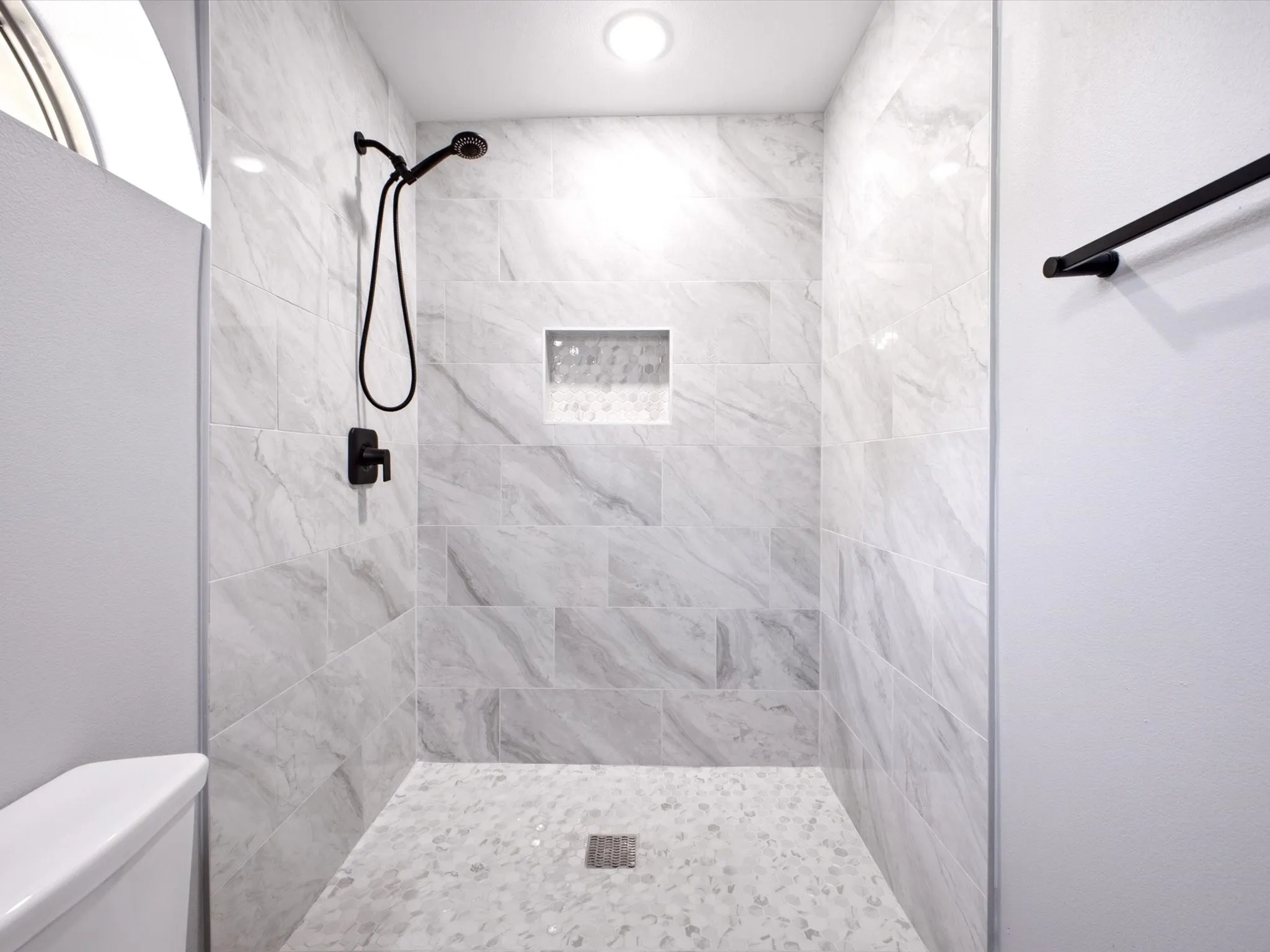 Walk-in shower with large format wall tiles, a built-in shower niche, and a mosaic tile floor