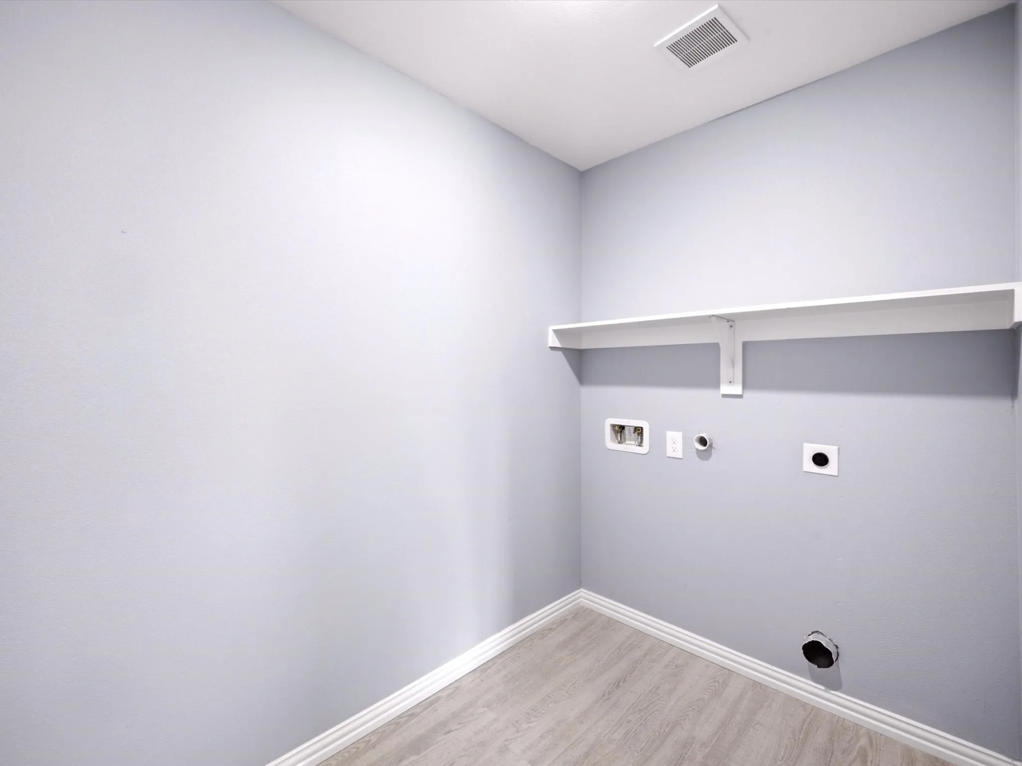 Laundry area featuring a built-in shelf, plumbing connections, electrical outlet, and wood-finish flooring