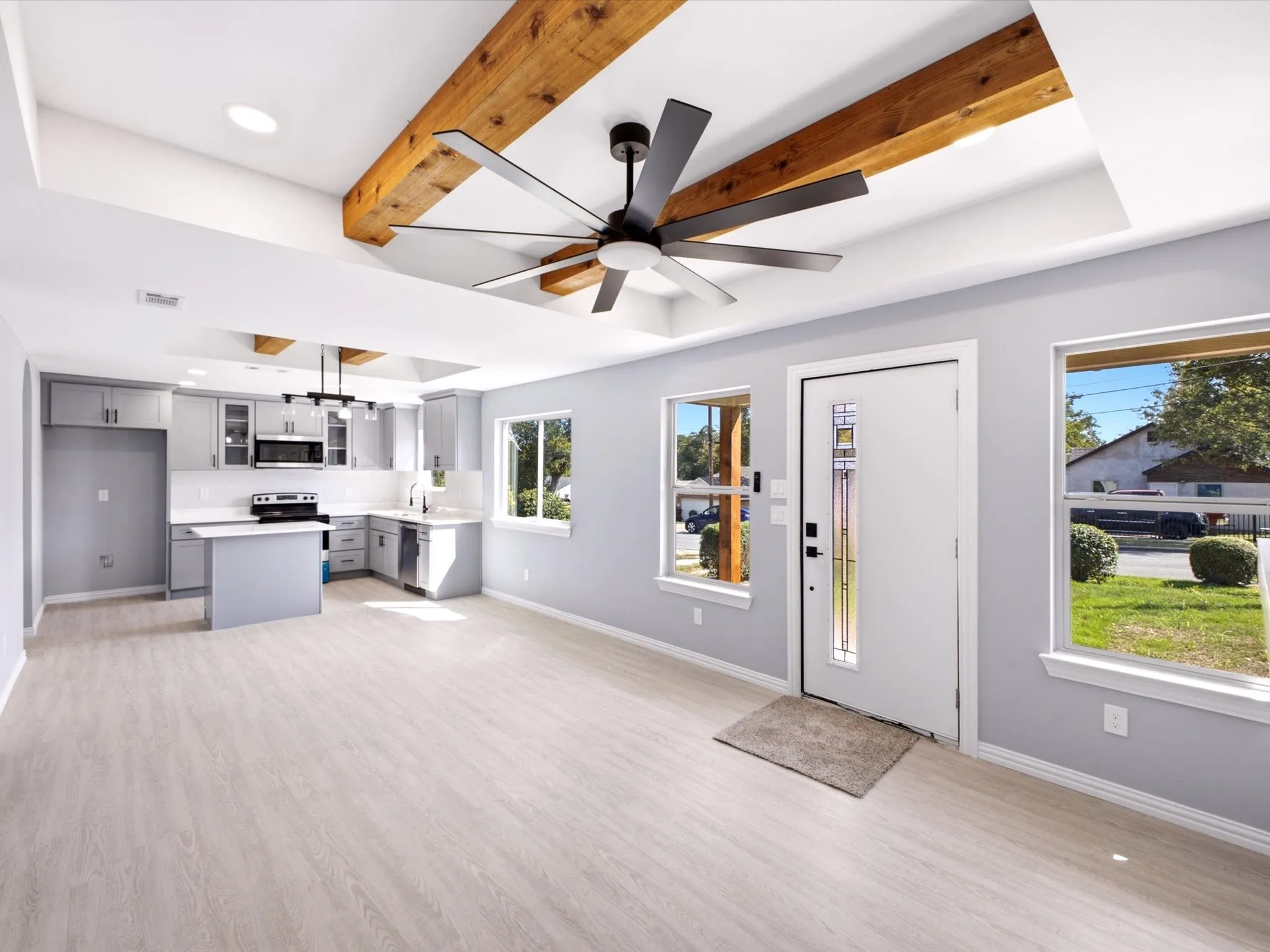 Light wood-finish flooring throughout, tray ceiling with exposed wood beams, and a modern ceiling fan