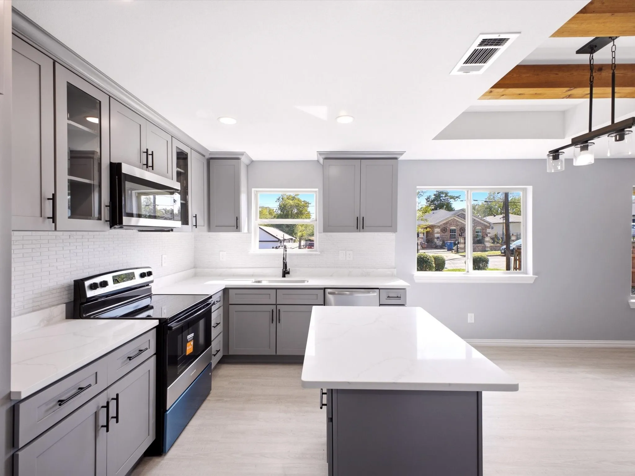 Kitchen featuring gray shaker-style cabinetry, white quartz countertops, a white subway tile backsplash, stainless steel appliances, and a central island with a waterfall edge