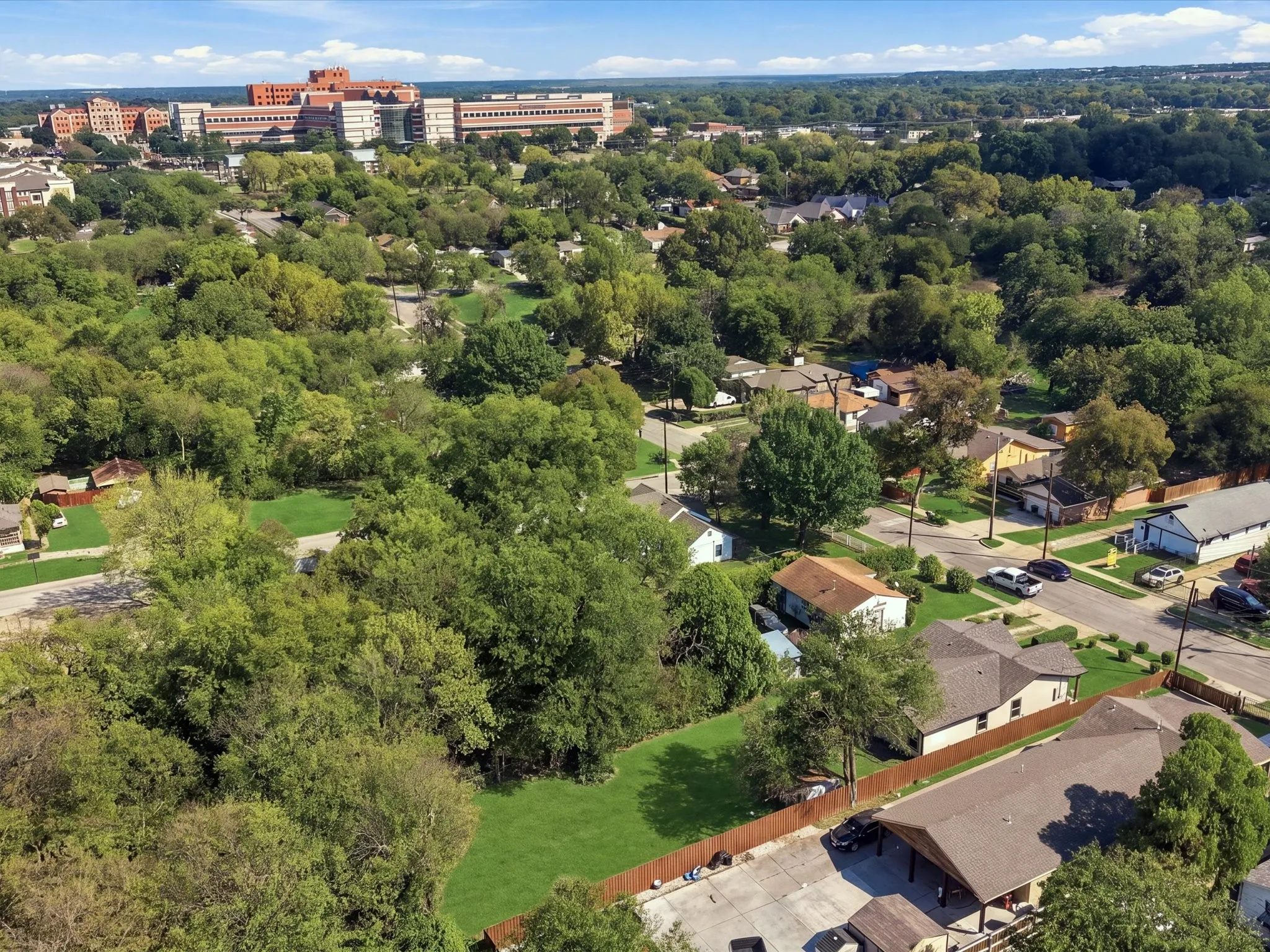 Expansive green space surrounded by mature trees, featuring residential properties and community infrastructure