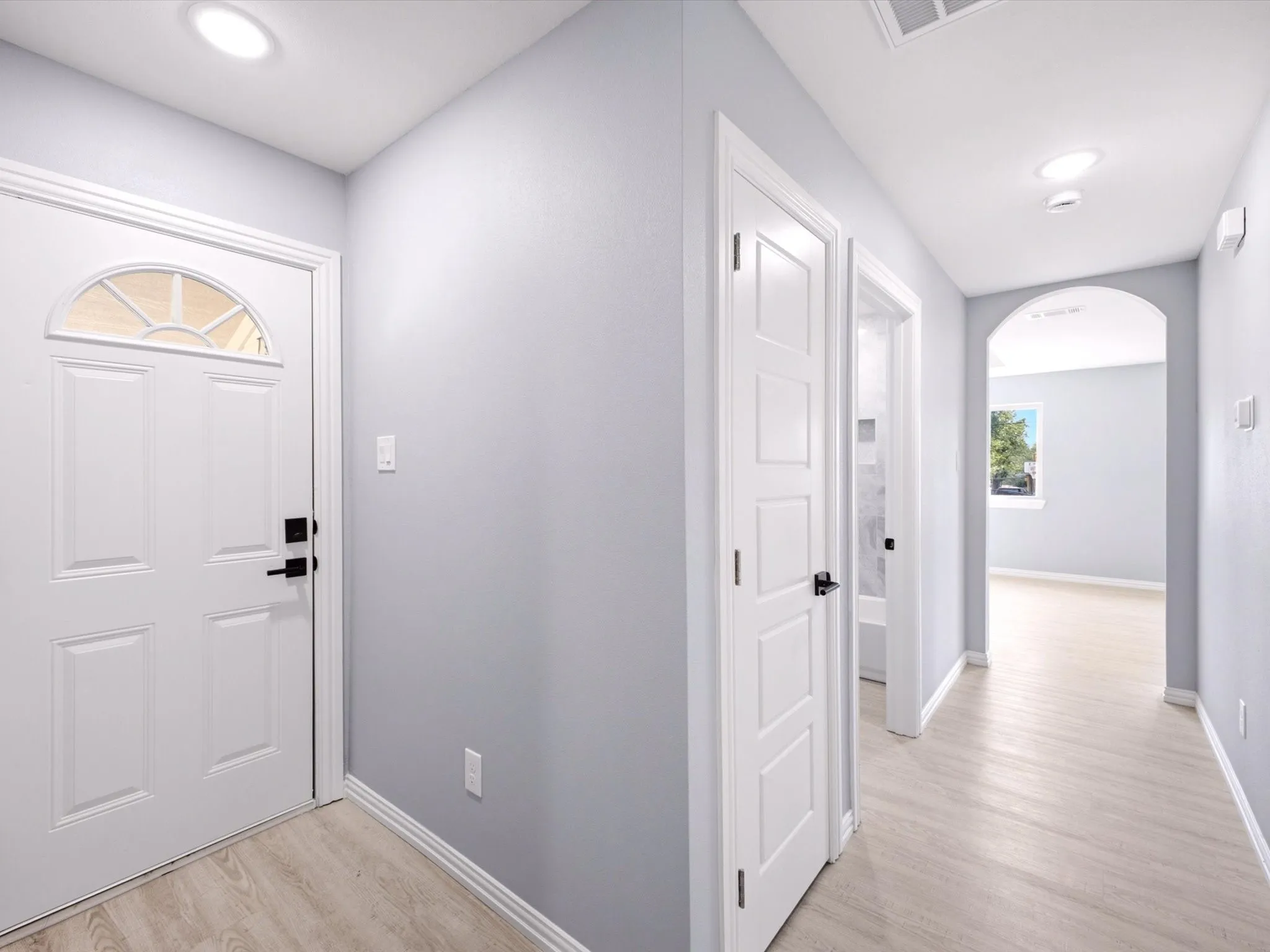 Recessed ceiling lighting, light wood-finish flooring, arched doorway, paneled interior doors, and front door with decorative glass insert