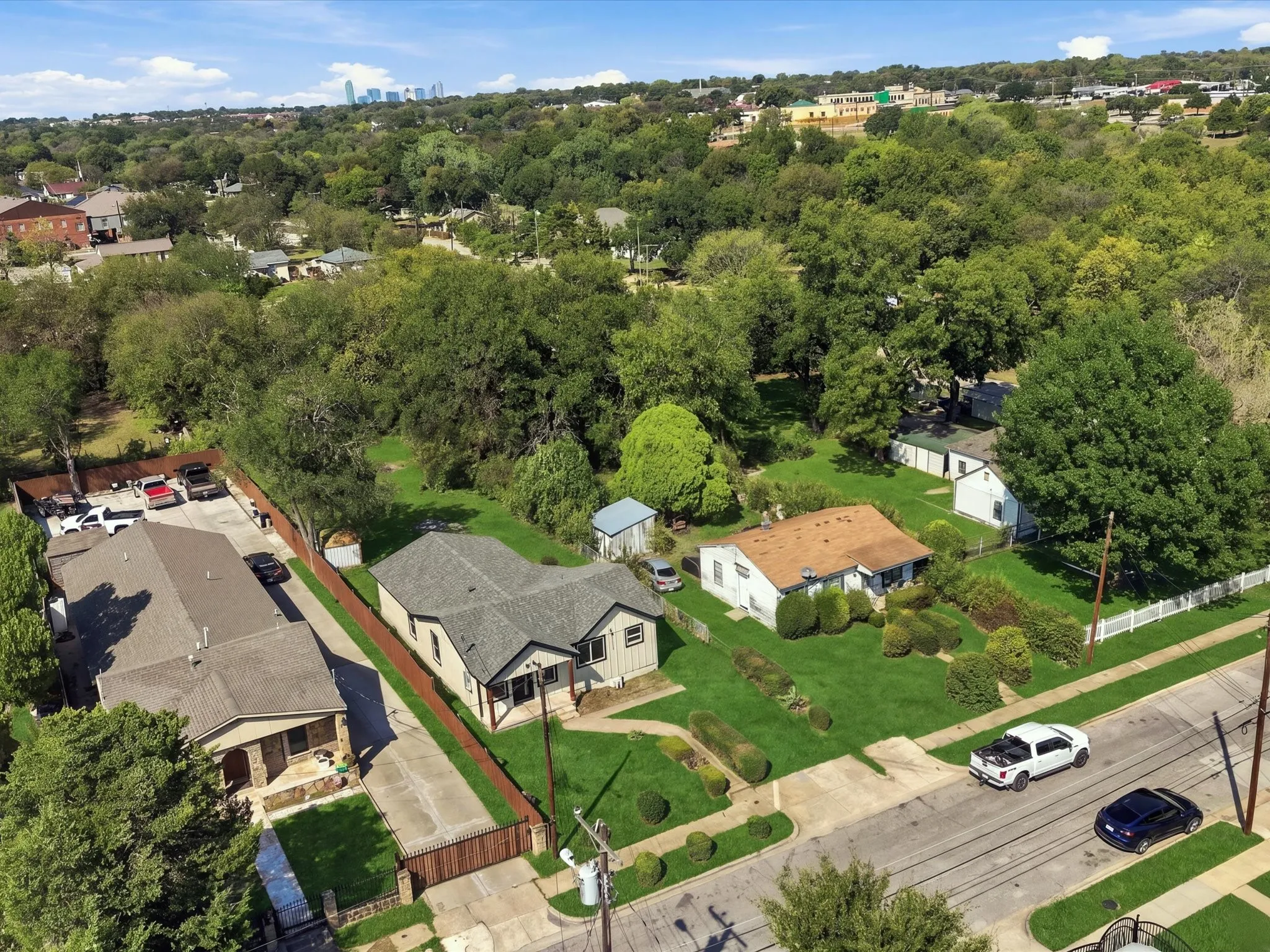 Aerial perspective showcasing multiple properties, extensive tree coverage, and distant urban buildings