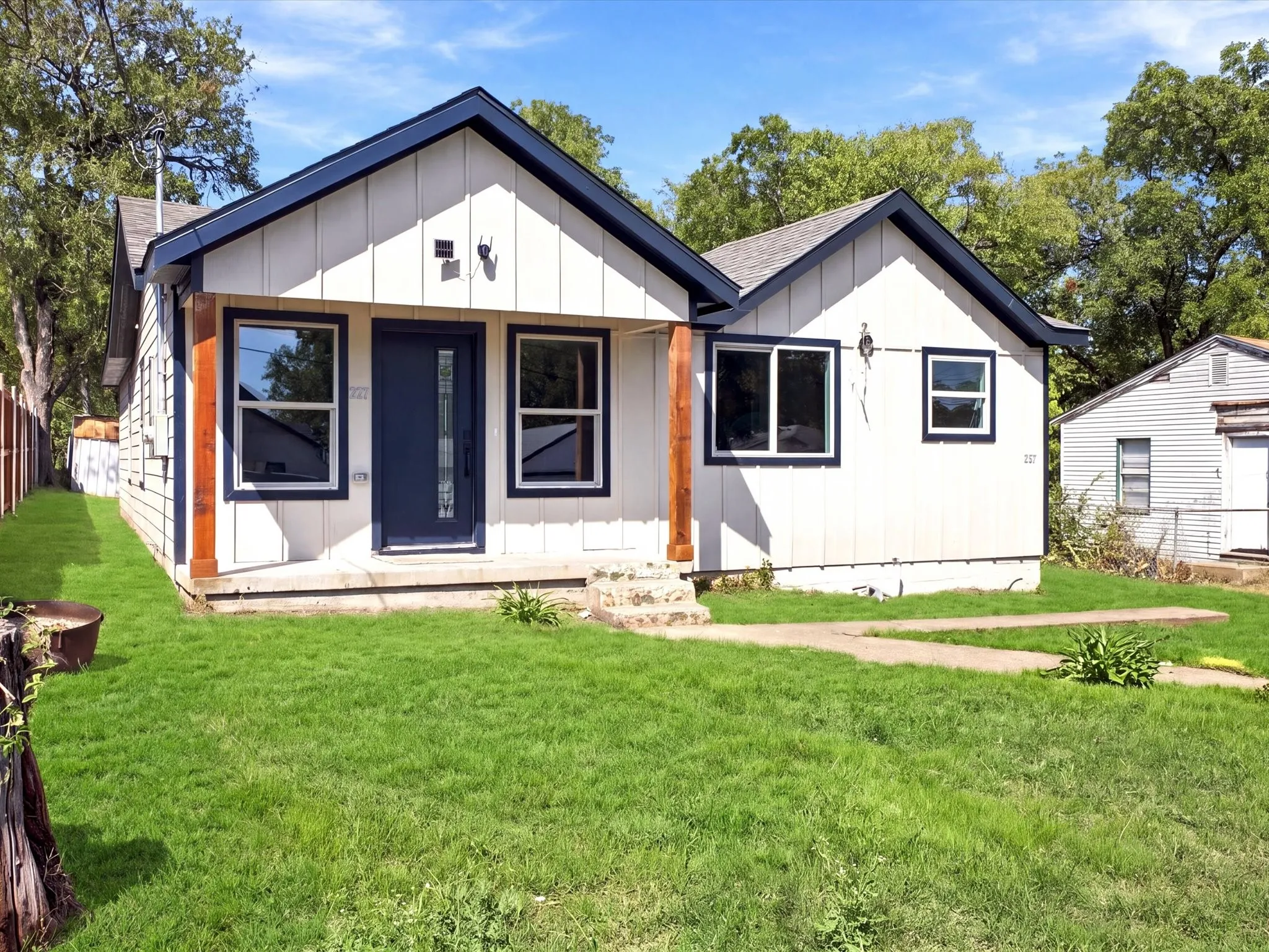 White exterior siding with dark trim, a dark entry door, a wood support post, and a concrete pathway