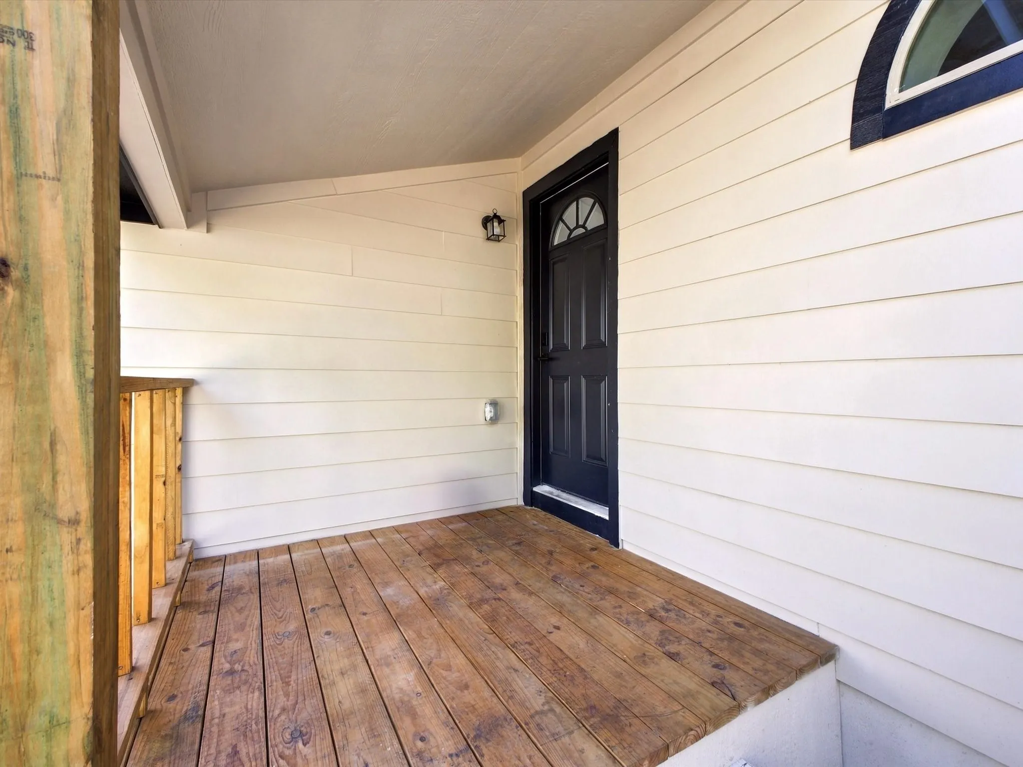 Covered porch with wood plank flooring and a dark entry door