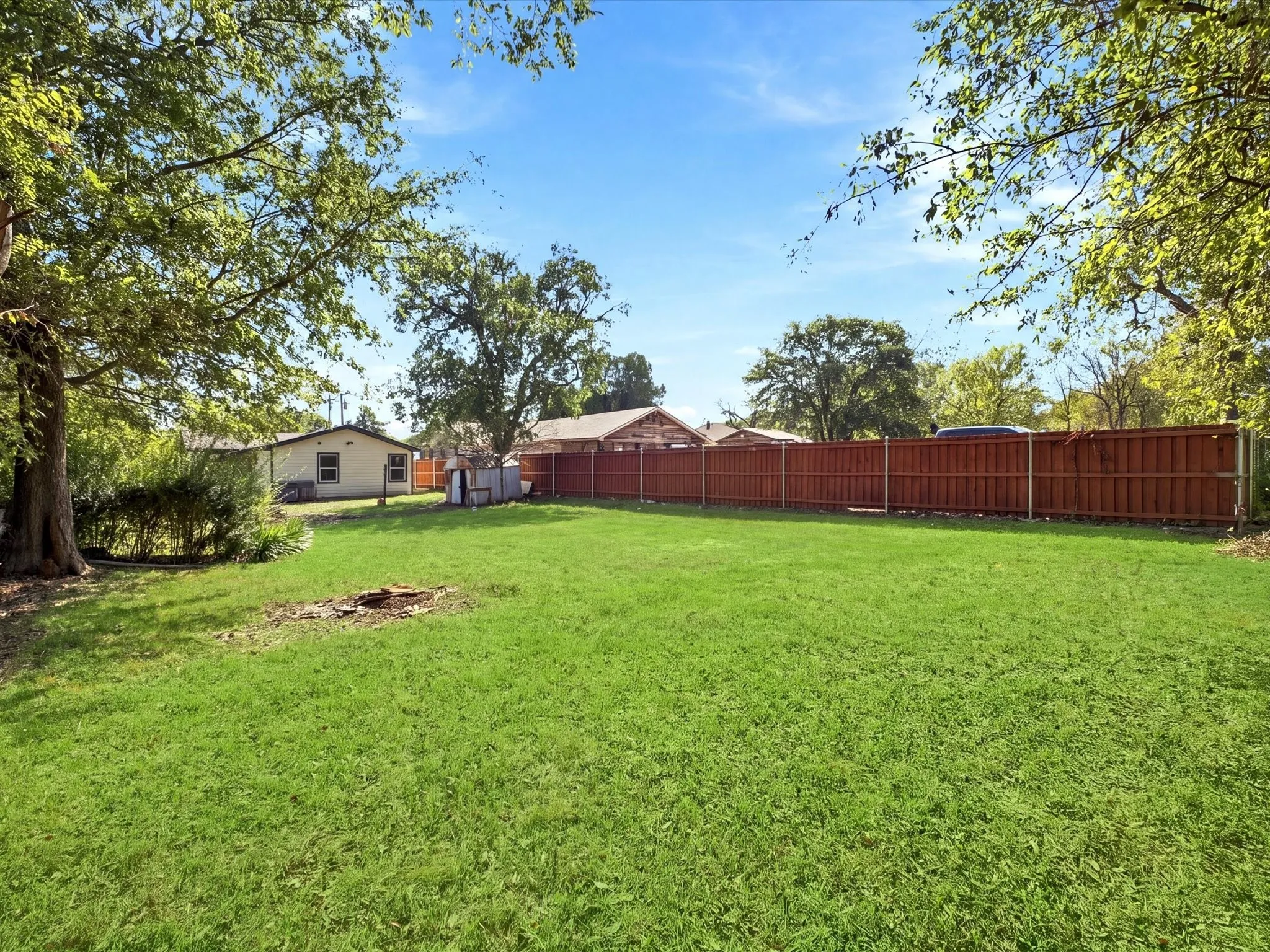 Expansive backyard featuring a manicured lawn, mature trees, and a privacy fence