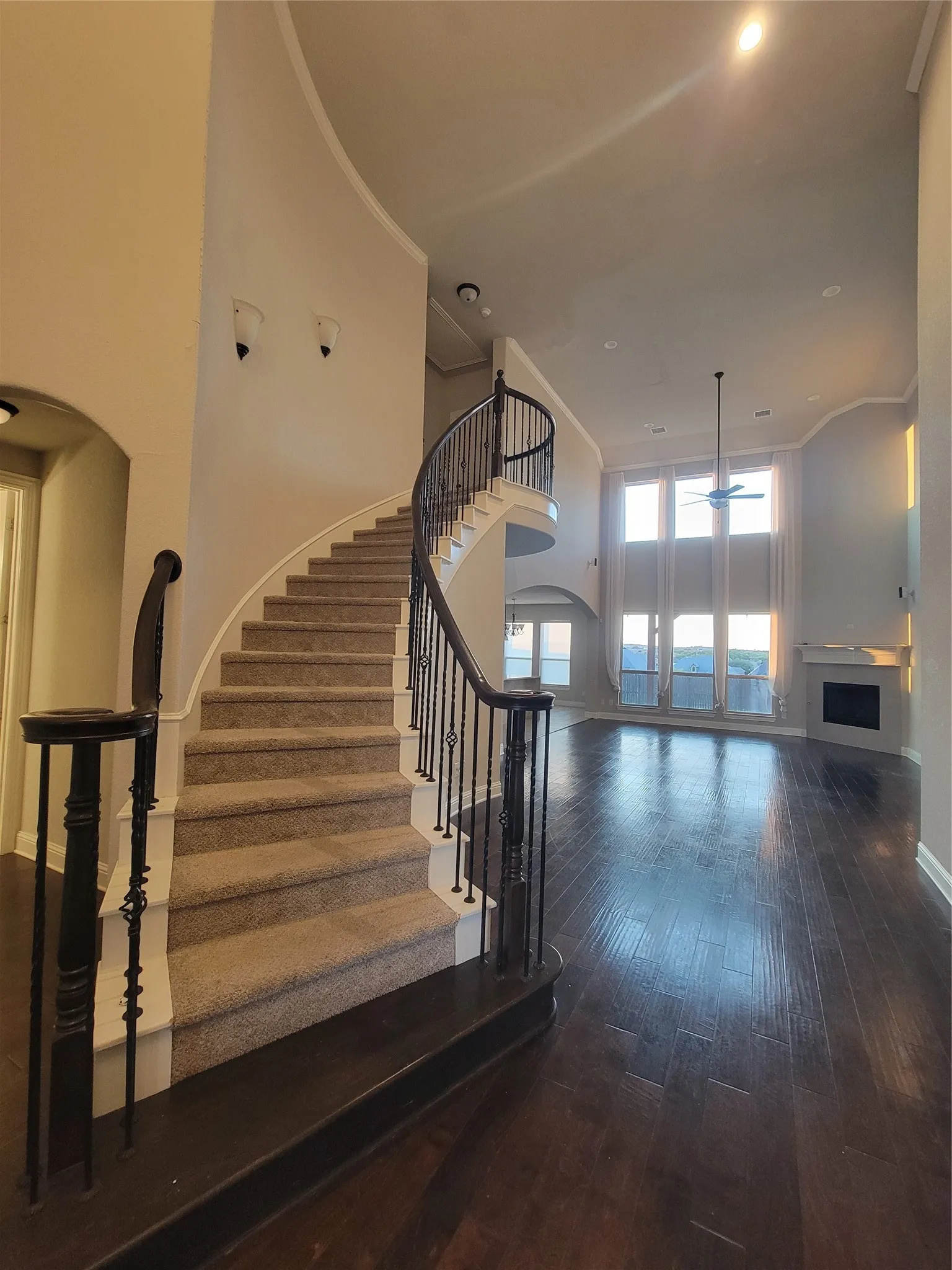 Curved staircase with decorative wrought iron spindles, dark wood-finish flooring, two-story windows, and a built-in fireplace