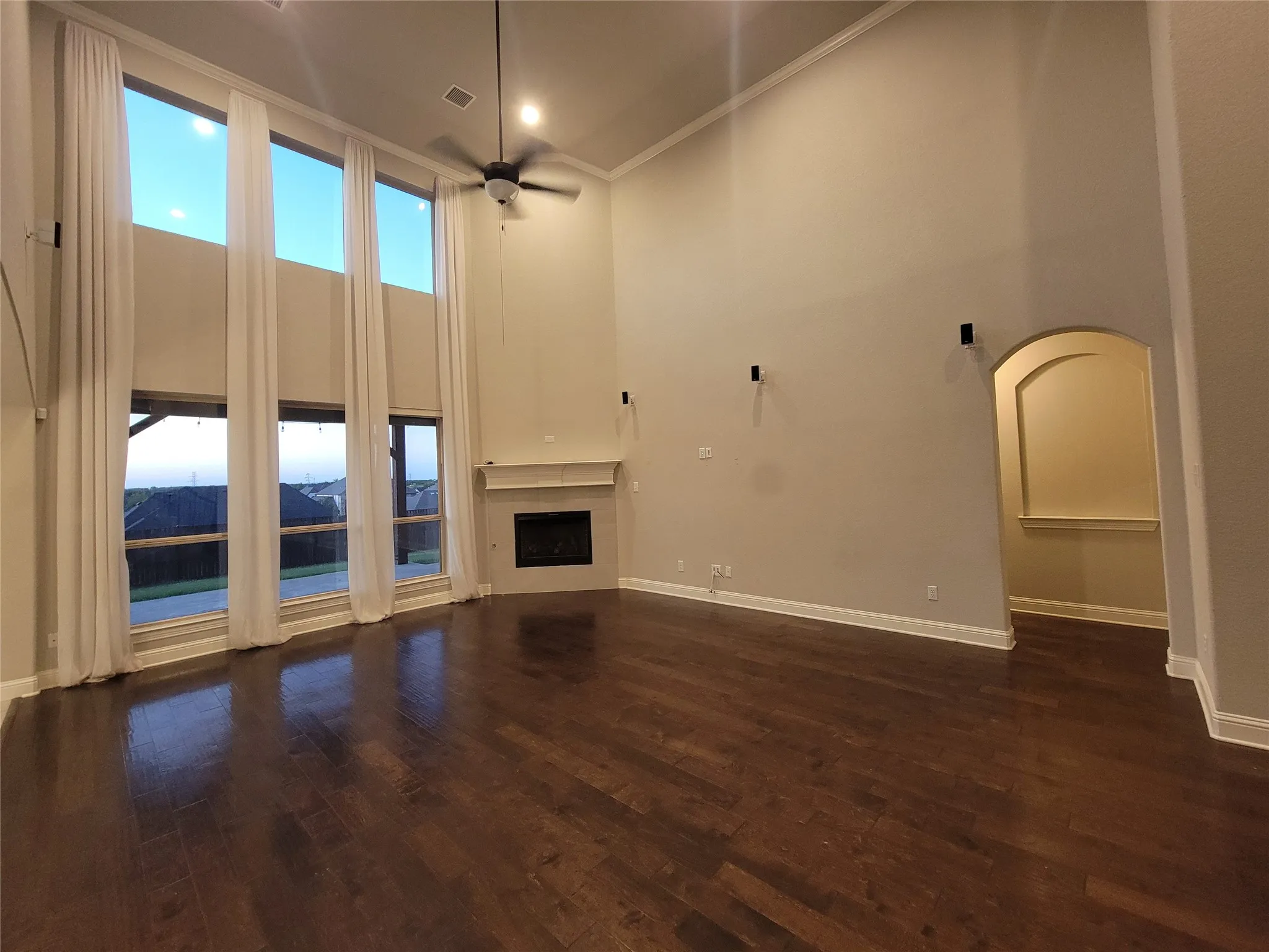 Vaulted ceiling with a ceiling fan, wood-finish flooring, a fireplace with a mantel, an arched entry, and expansive windows