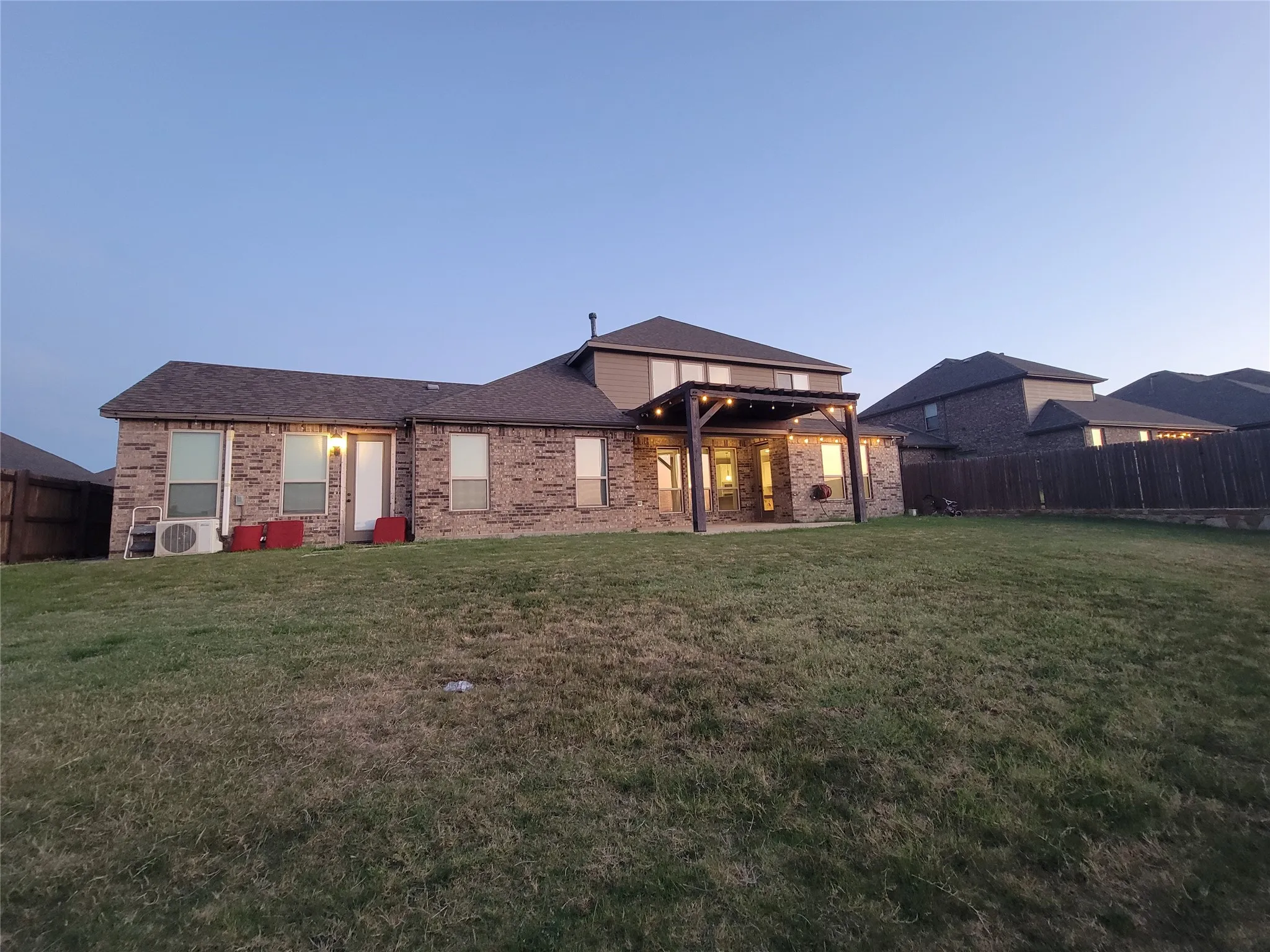 Expansive rear yard featuring a covered patio with a pergola, brick exterior, and a privacy fence