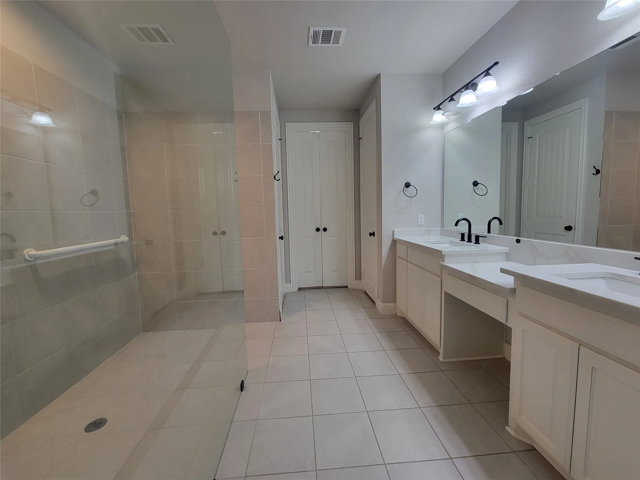 Spacious bathroom featuring a dual vanity with white cabinetry, light-toned countertops, and matte black fixtures
