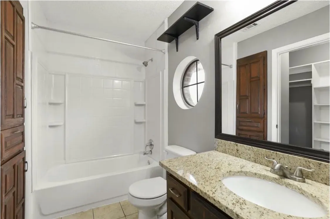 Bathroom featuring a shower-tub combination, a round window, a vanity with a granite countertop, and a built-in storage cabinet