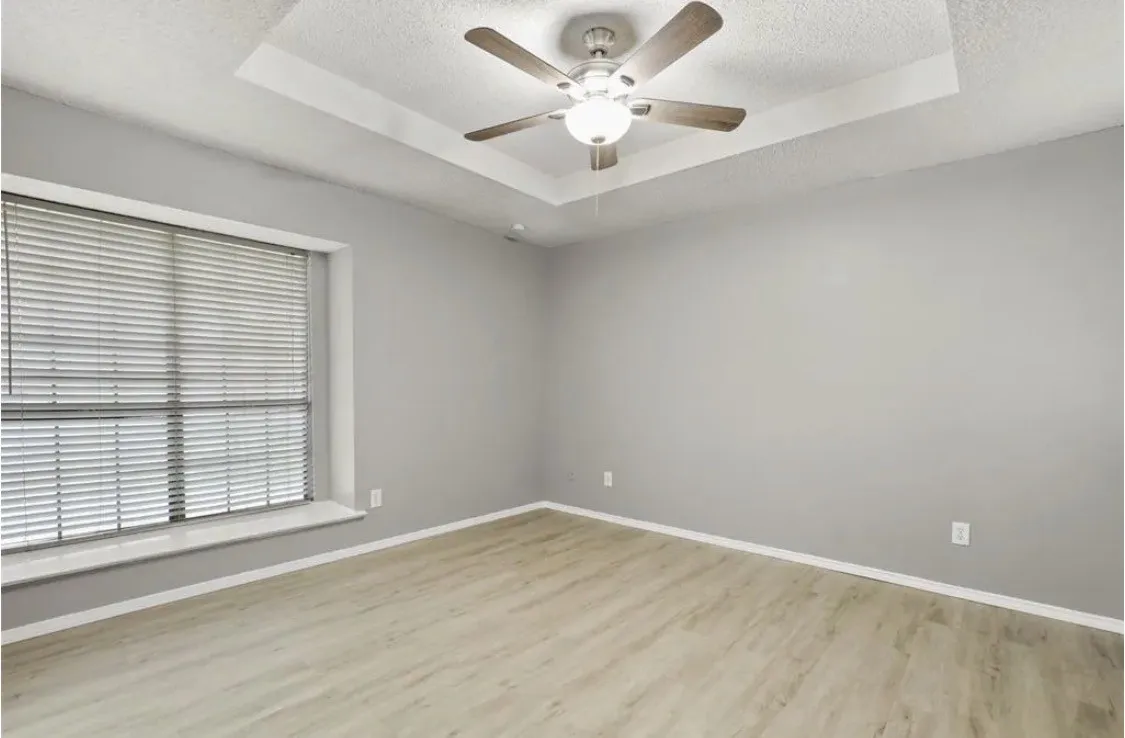 Tray ceiling with a ceiling fan light fixture, wood-finish flooring, and a window with blinds