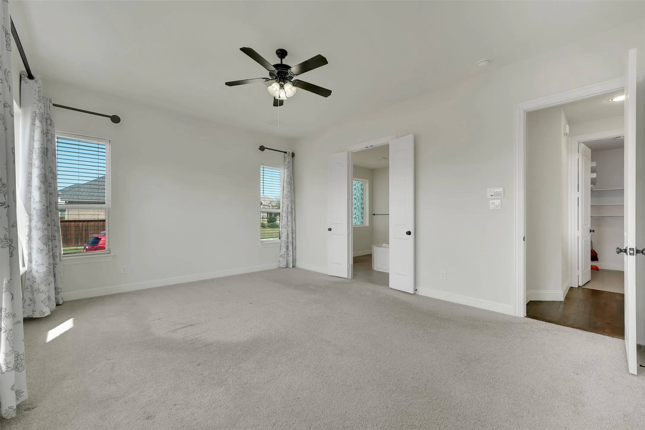 Spacious room featuring light-colored carpeting, two windows with blinds, and a ceiling fan with integrated lighting