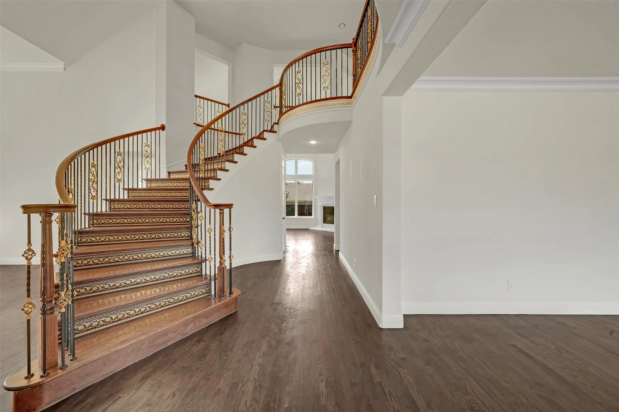 Curved staircase with wrought iron balusters and ornate detailing, wood-finish flooring, crown molding, and high ceilings